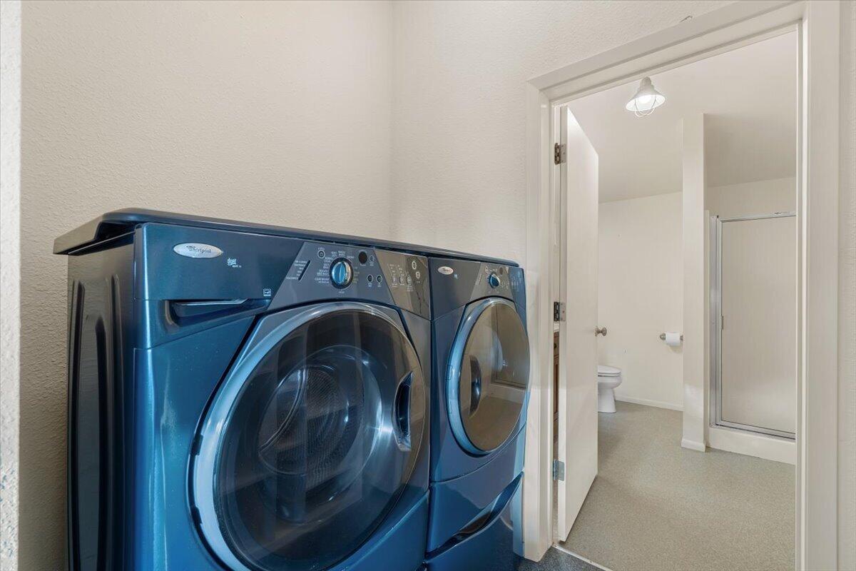 Laundry area with blue front-loading washer and dryer beside an open bathroom doorway.