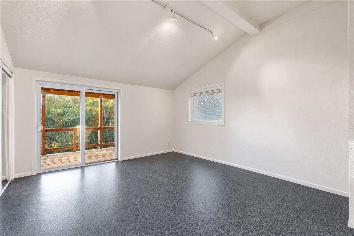 Empty room with dark gray flooring and sliding glass doors opening onto a wooded deck.