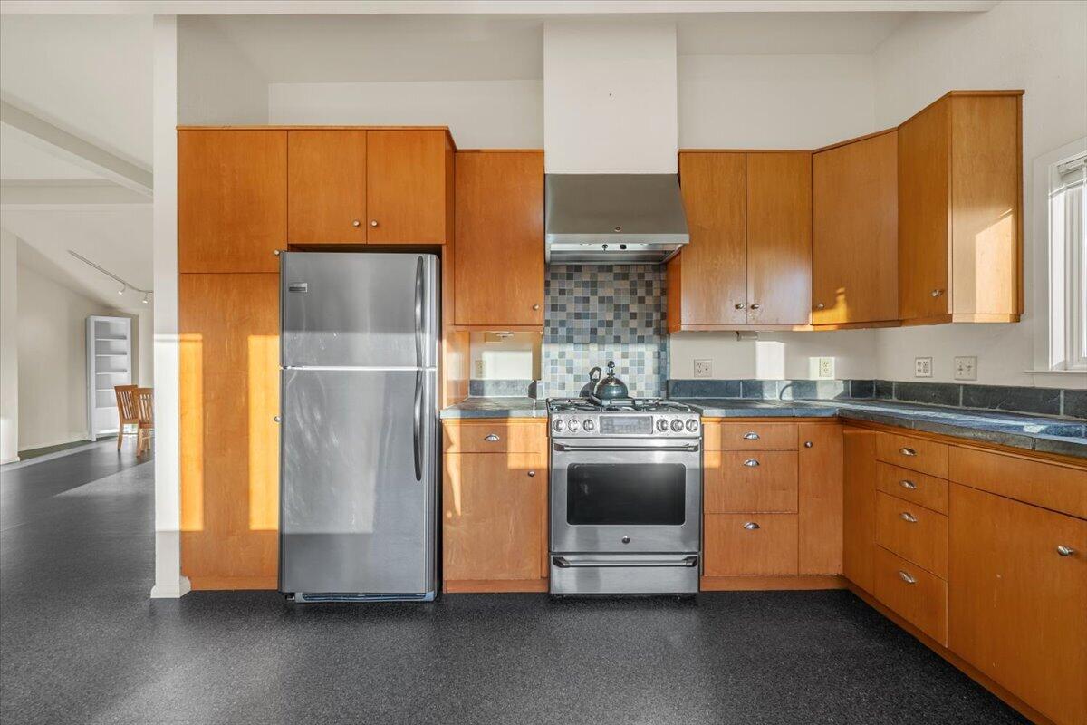 Kitchen with warm wood cabinets, stainless-steel appliances, and a multicolored tile backsplash.