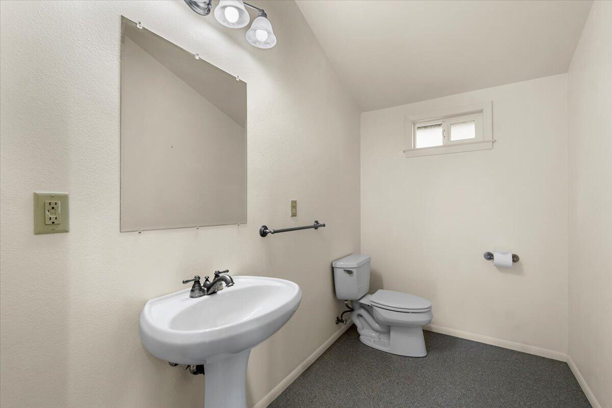 Bathroom with a pedestal sink, toilet, large mirror, and small high window.