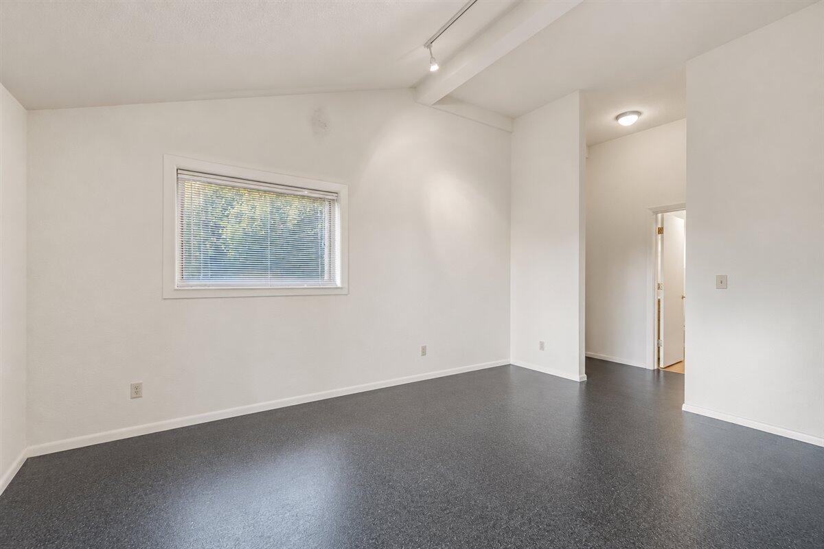 Vacant room with dark gray flooring, a window with blinds, and an open doorway.