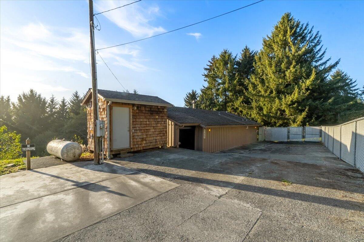 Wood-sided property with an attached garage, fenced paved driveway, and evergreen trees.