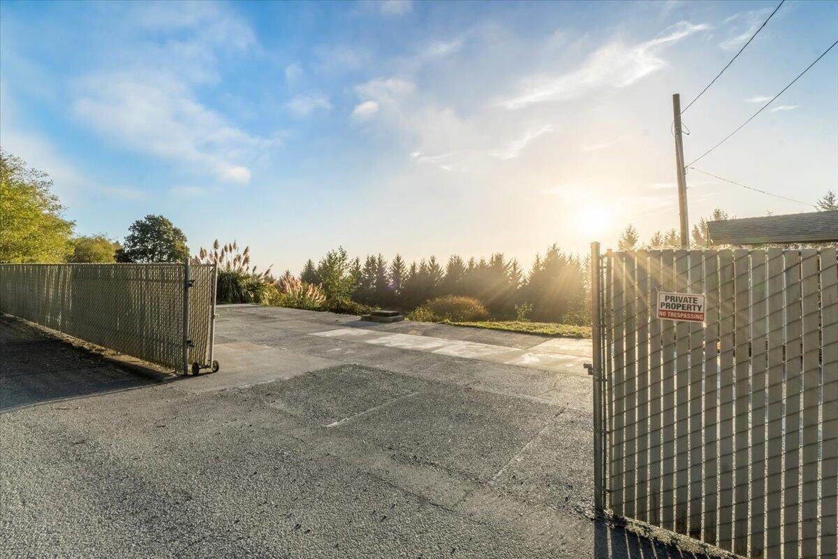 Paved driveway entrance with open metal gates and a private property sign in warm evening light.