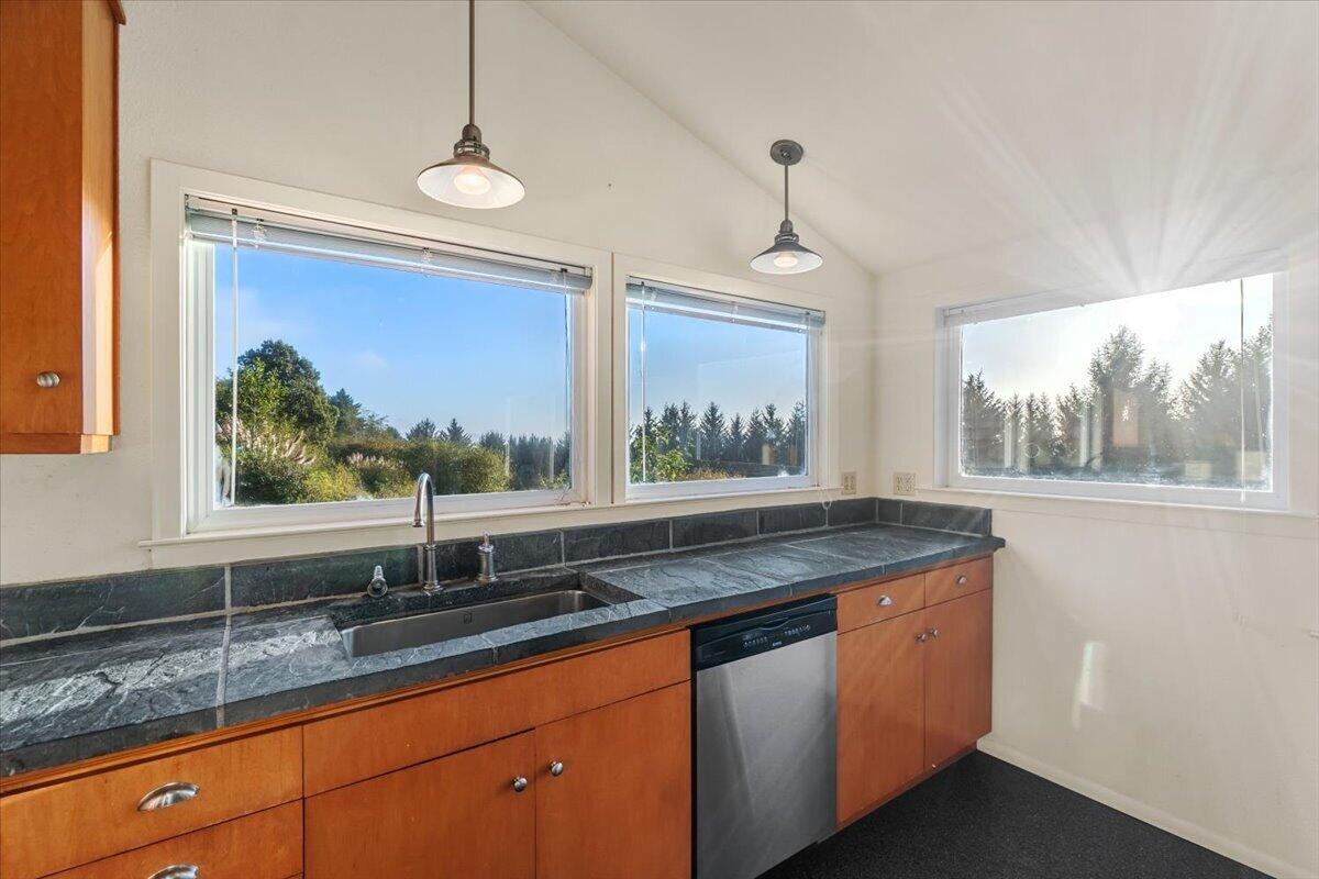 Kitchen with warm wood cabinets, dark stone counters, and large windows overlooking trees.