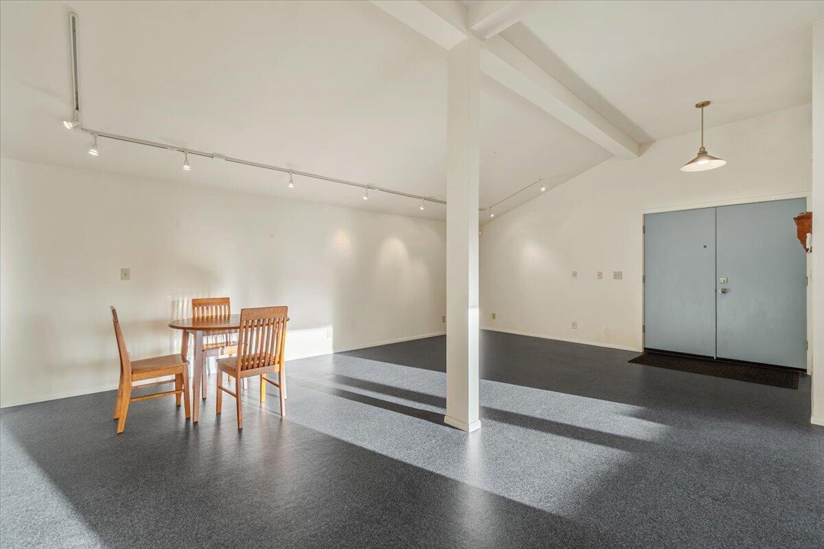 Open carpeted interior with vaulted ceiling, central support column, and blue-gray double entry doors.