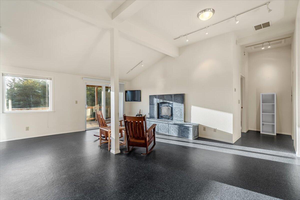 Living room with a vaulted ceiling, stone fireplace, dark floors, and sliding glass door to a deck.