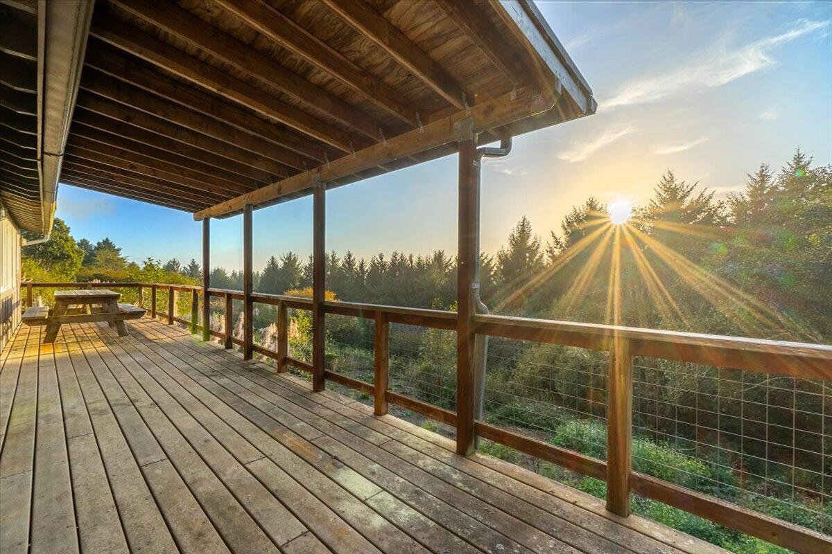 Covered wooden deck with a picnic table overlooking trees in golden-hour sunlight.