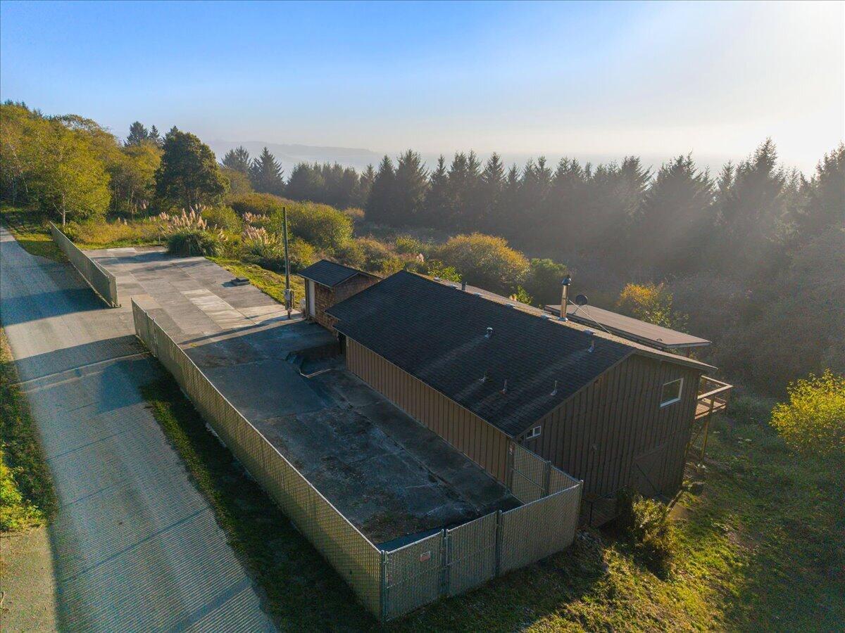 Aerial view of a brown home and fenced paved area amid trees in warm evening light.