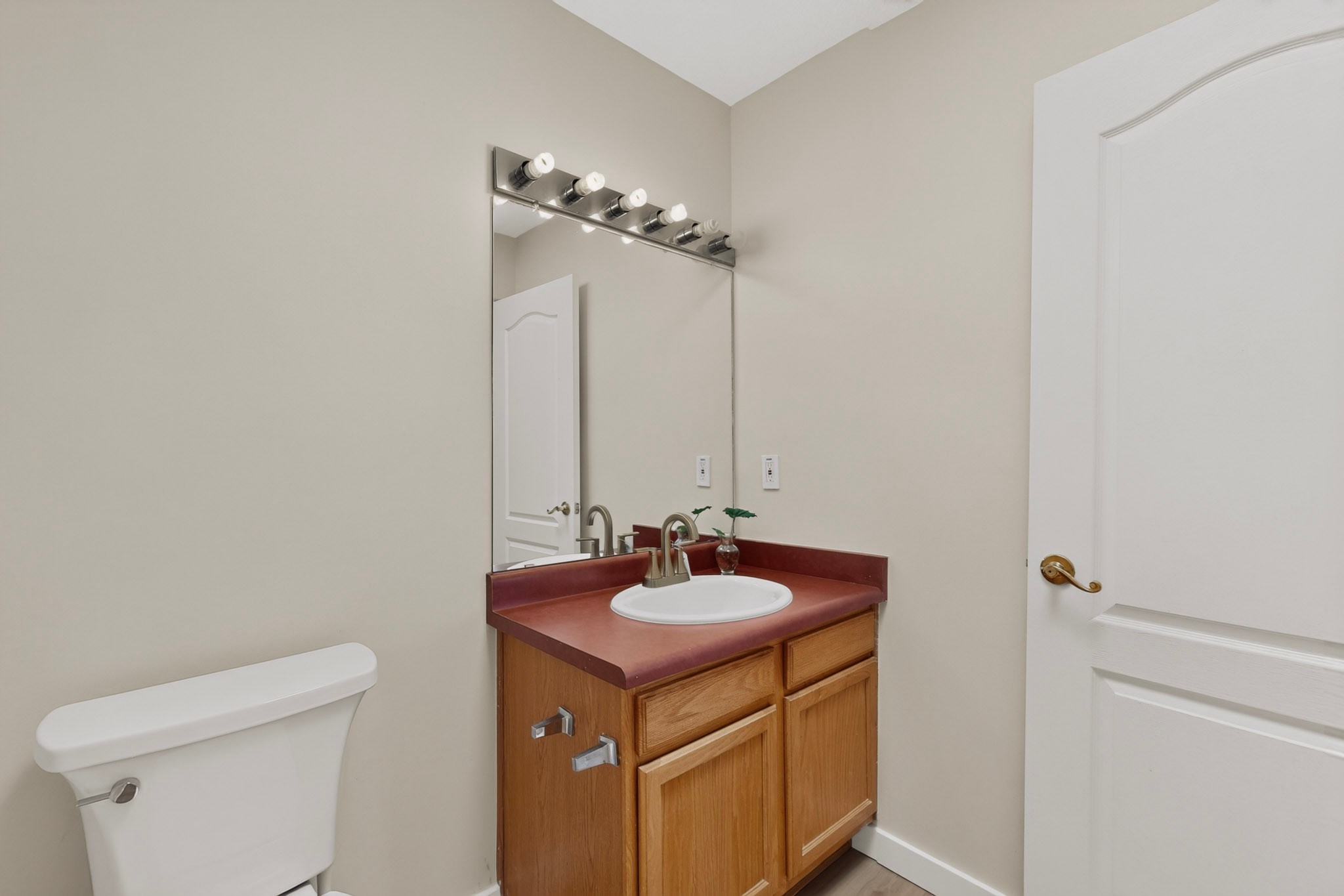 Bathroom vanity with a reddish countertop, wood cabinetry, oval sink, and adjacent toilet.
