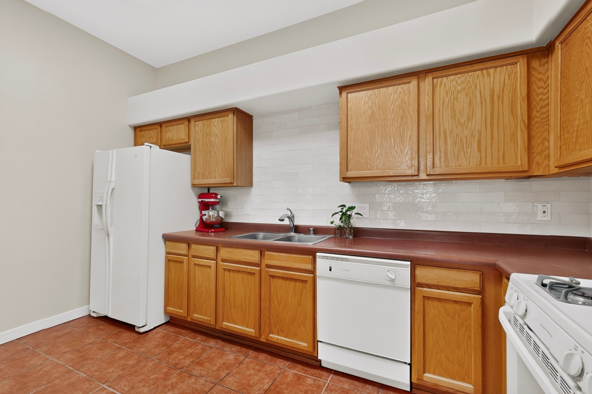 Kitchen with honey-colored cabinets, terracotta tile flooring, and white appliances.