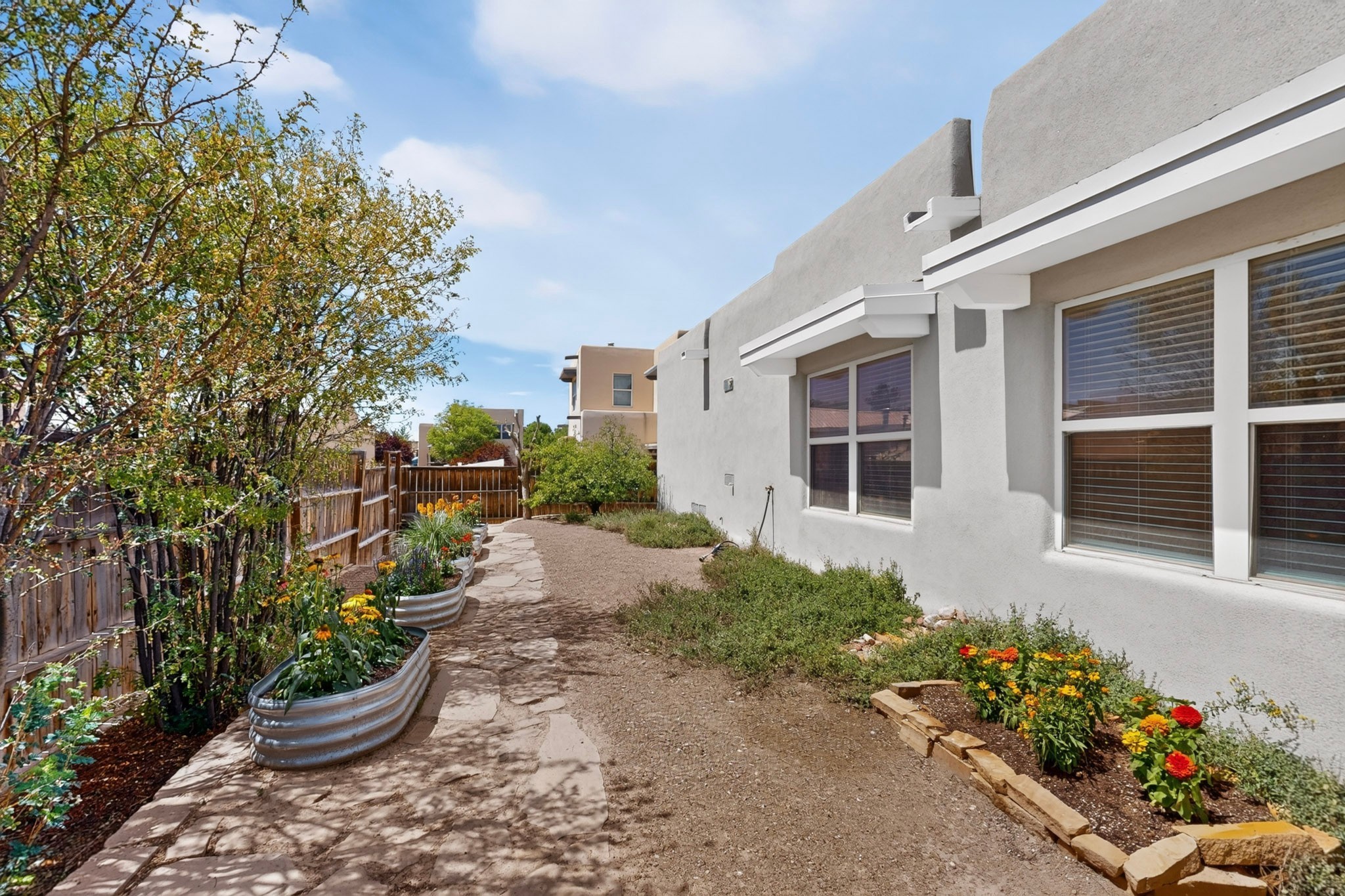 Home side yard with a stone walkway, raised garden beds, and colorful flowers.