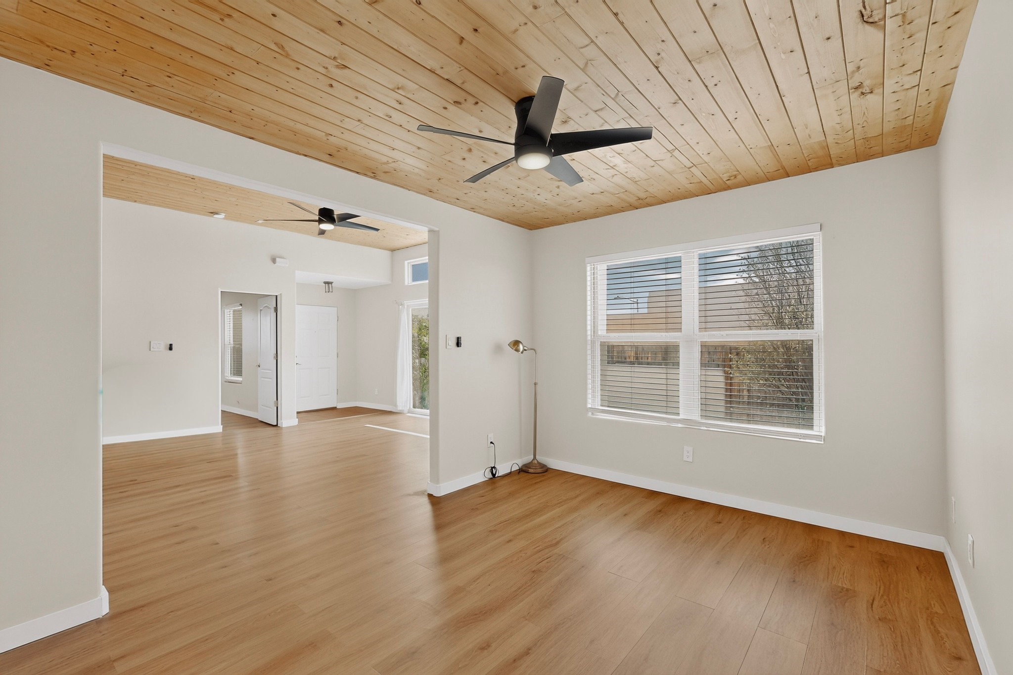 Empty living room with wood-plank ceiling, hardwood floors, and a large window with blinds.