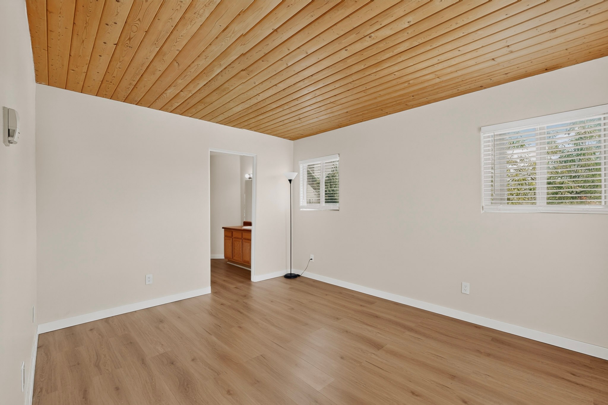 Empty room with a high wood-plank ceiling, wood-look floor, and two windows with blinds.