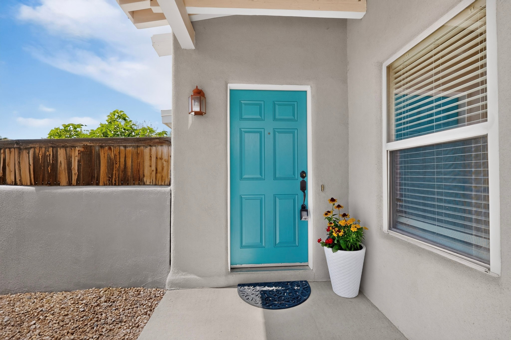 Home entry with a bright turquoise door, flower planter, and window with blinds.