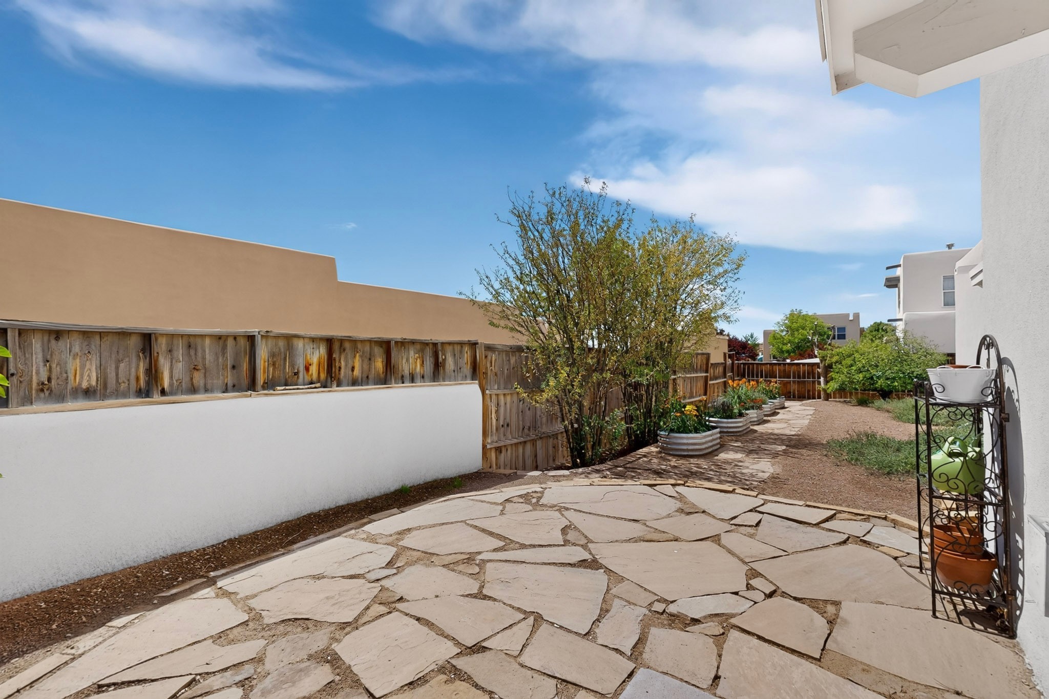 Backyard patio with a flagstone walkway, raised planters, and a leafy tree.