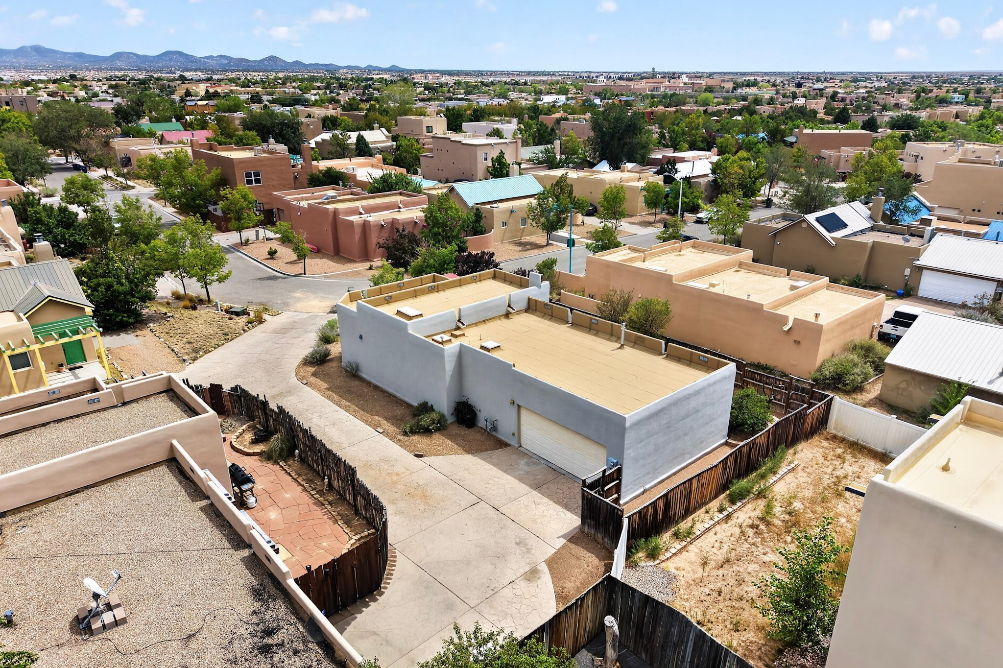 Aerial view of a flat-roofed home with fenced yard and mountains beyond the Santa Fe neighborhood.