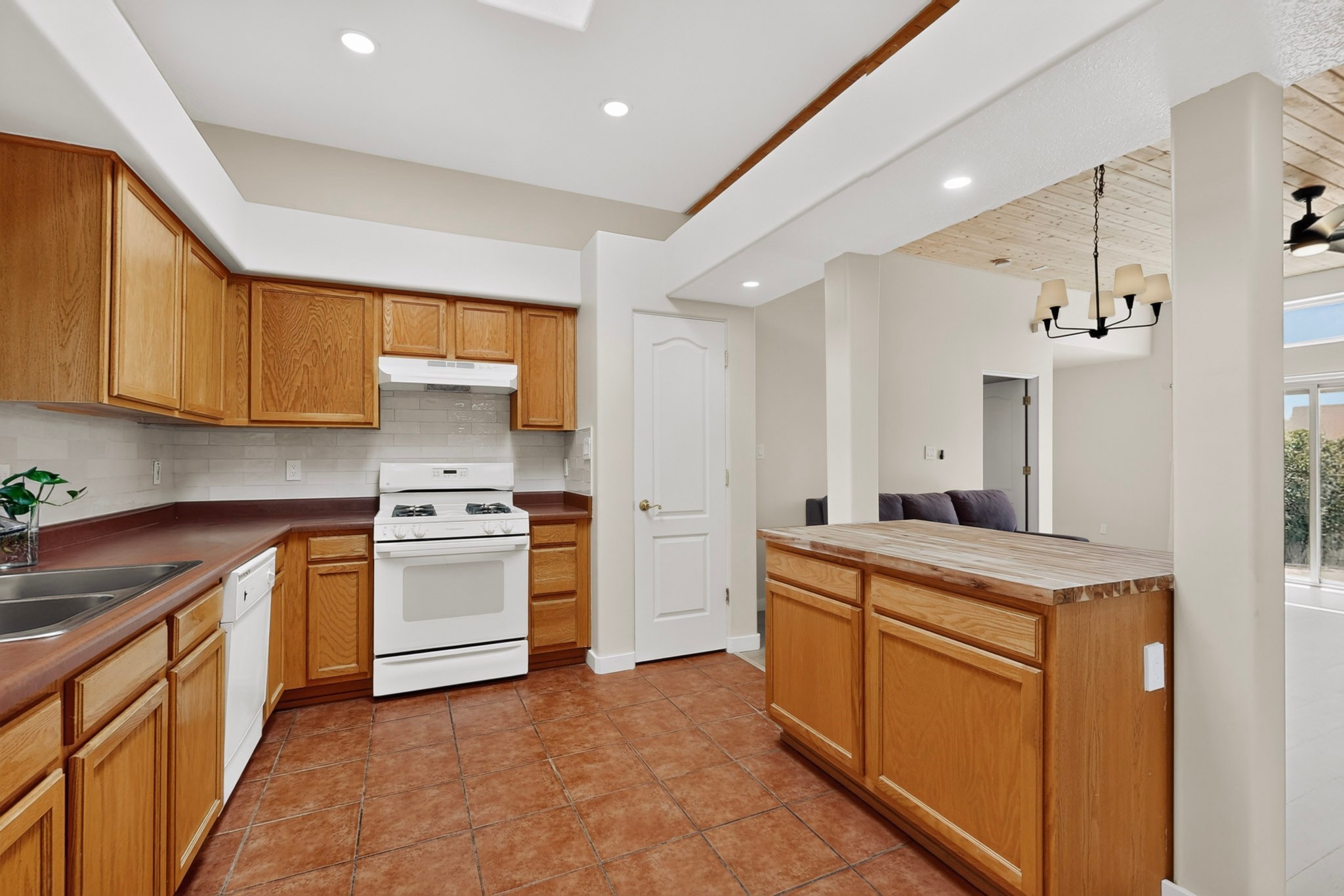 Kitchen with wood cabinets, tile floors, white appliances, and a central island beside the open living area.