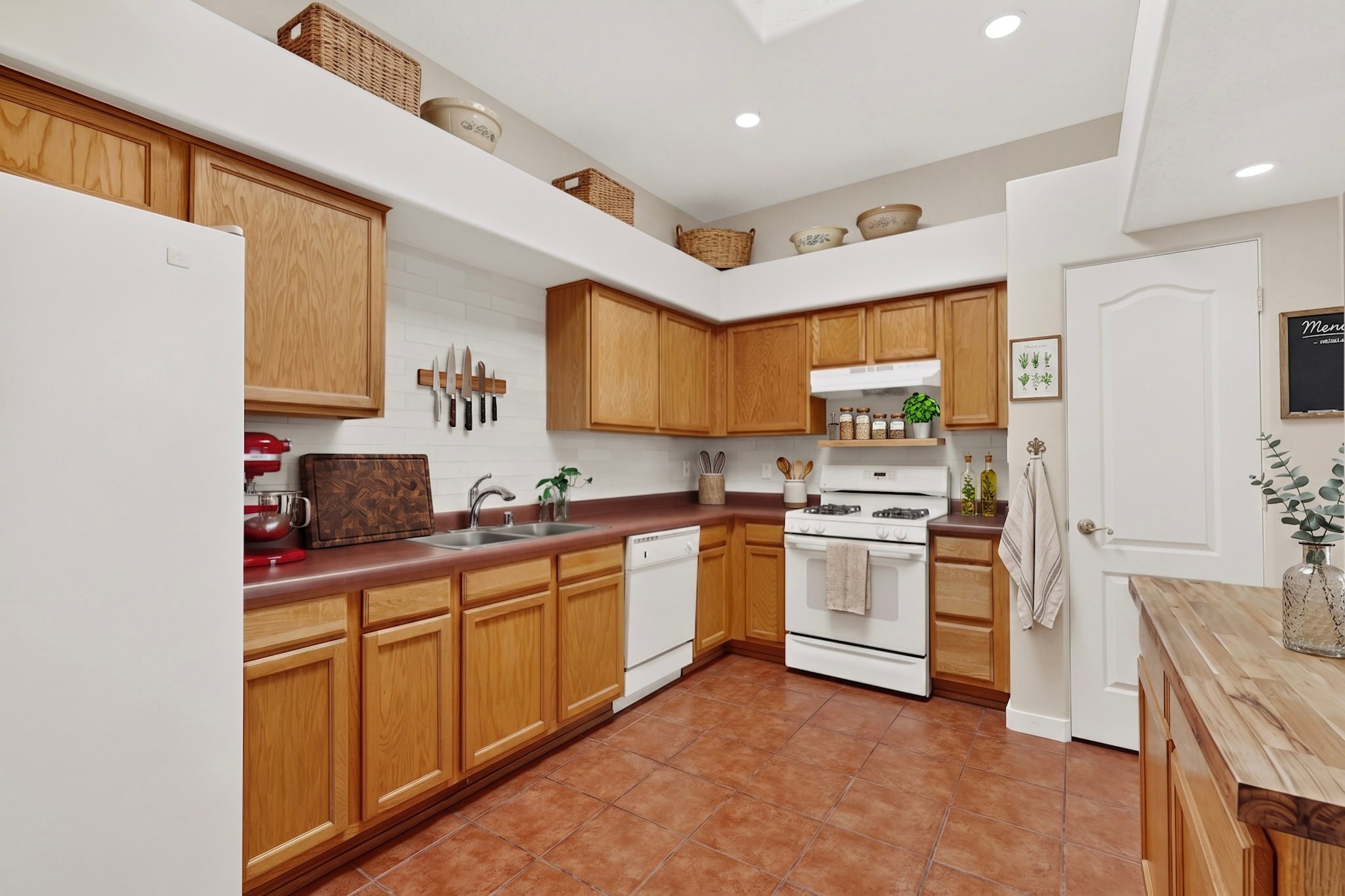 Kitchen with honey-colored cabinets, terracotta tile, and white appliances.