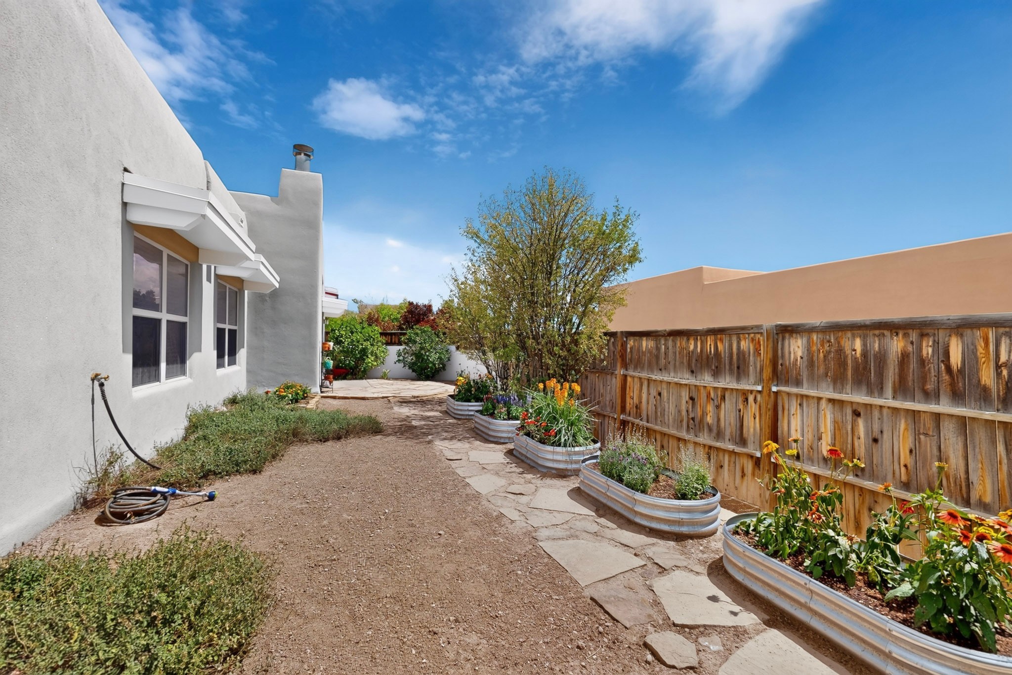 Side yard with raised flower beds and a stone path beside a wooden privacy fence.