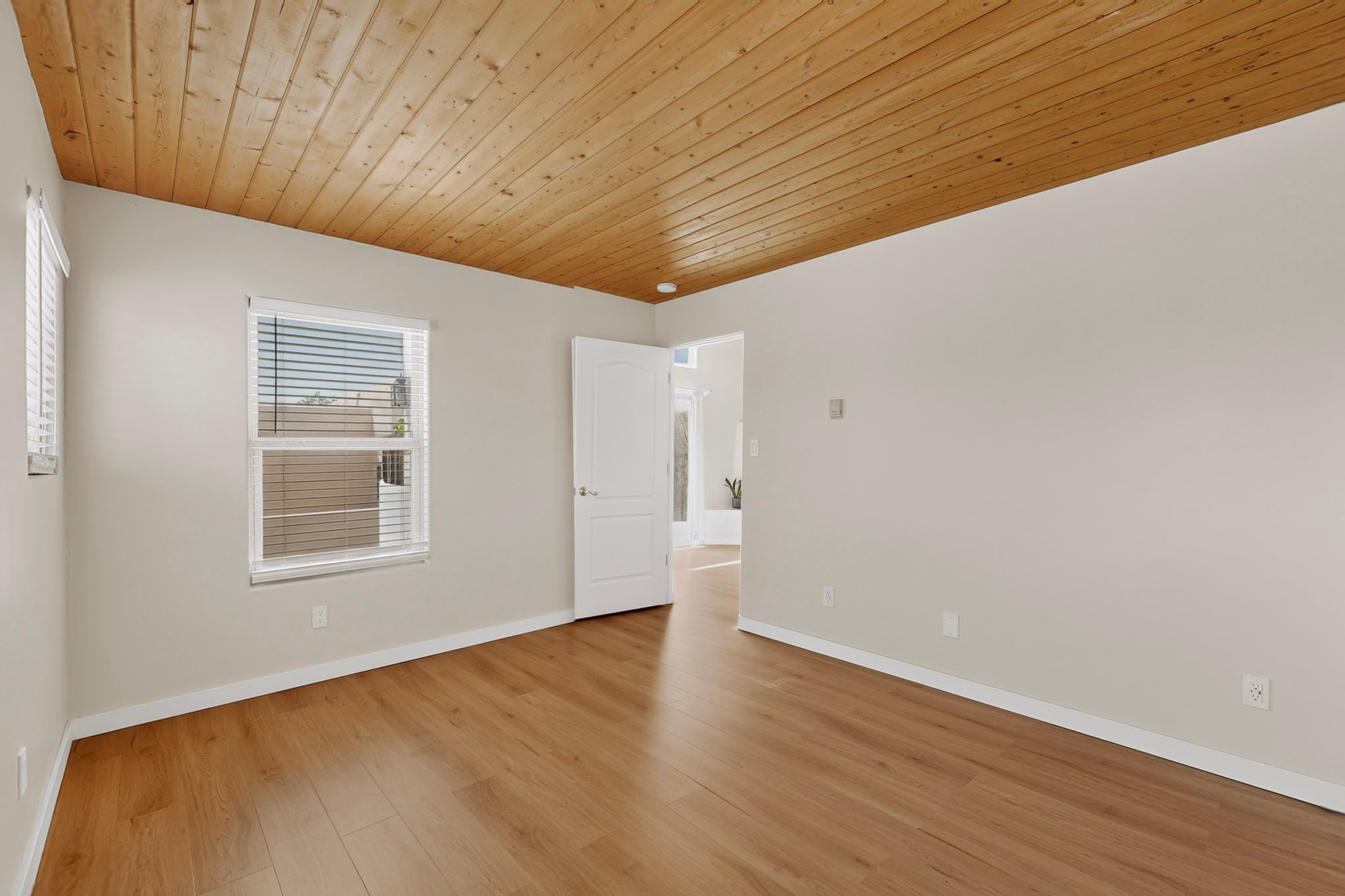 Empty room with wood flooring and a high, sloped wood-plank ceiling.