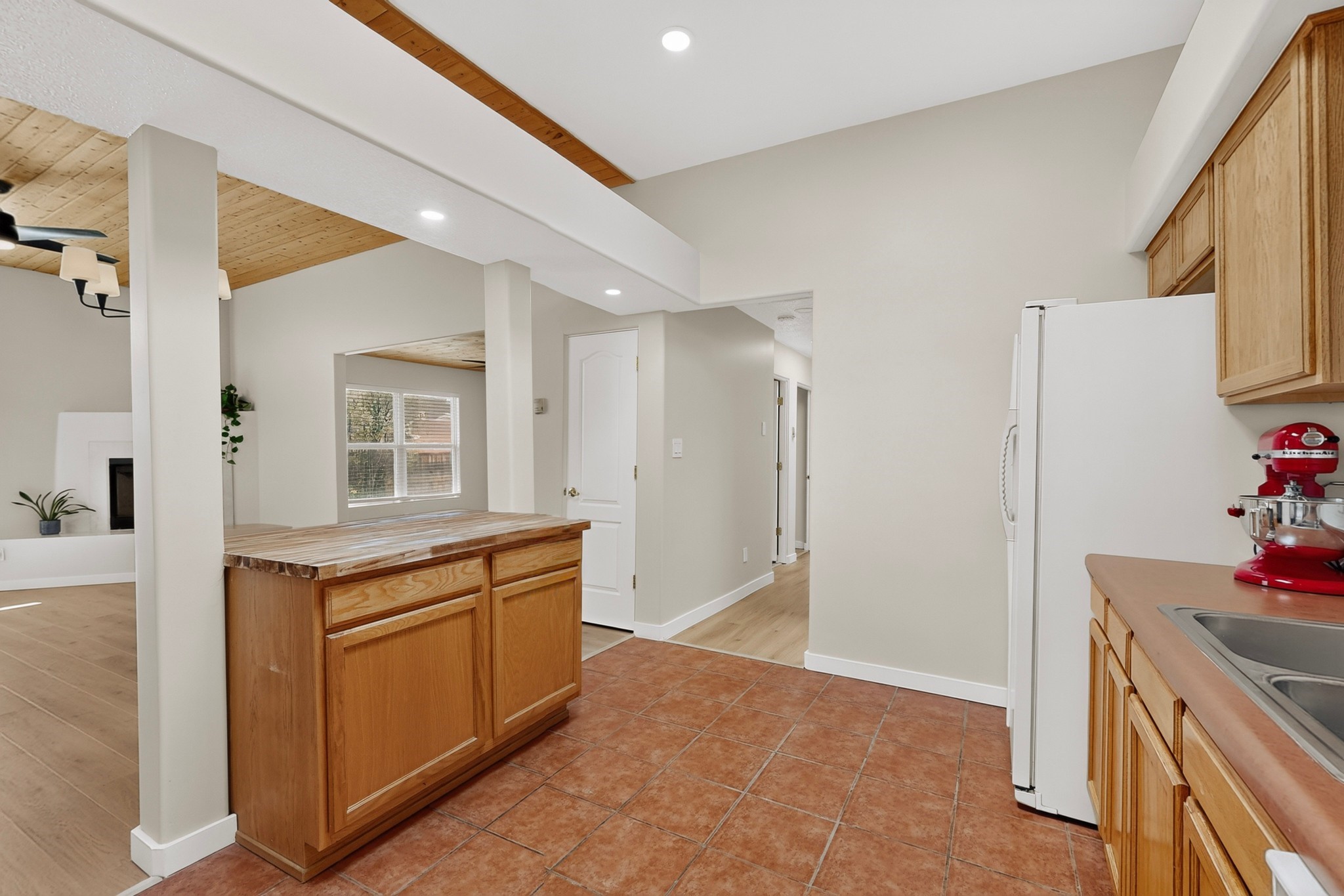 Kitchen with terracotta tile flooring, a wooden island, and exposed wood ceiling beams.