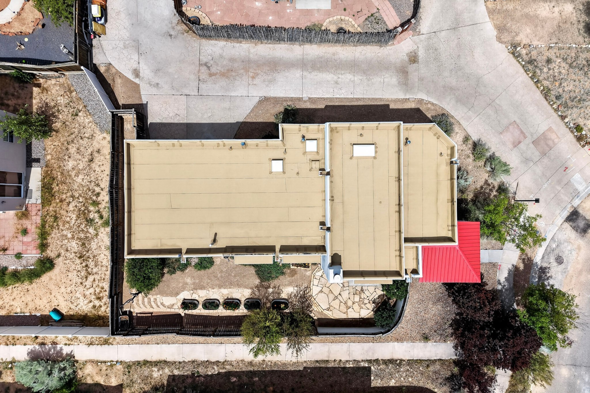 Aerial view of a home with a broad tan flat roof and a red metal-roofed section.