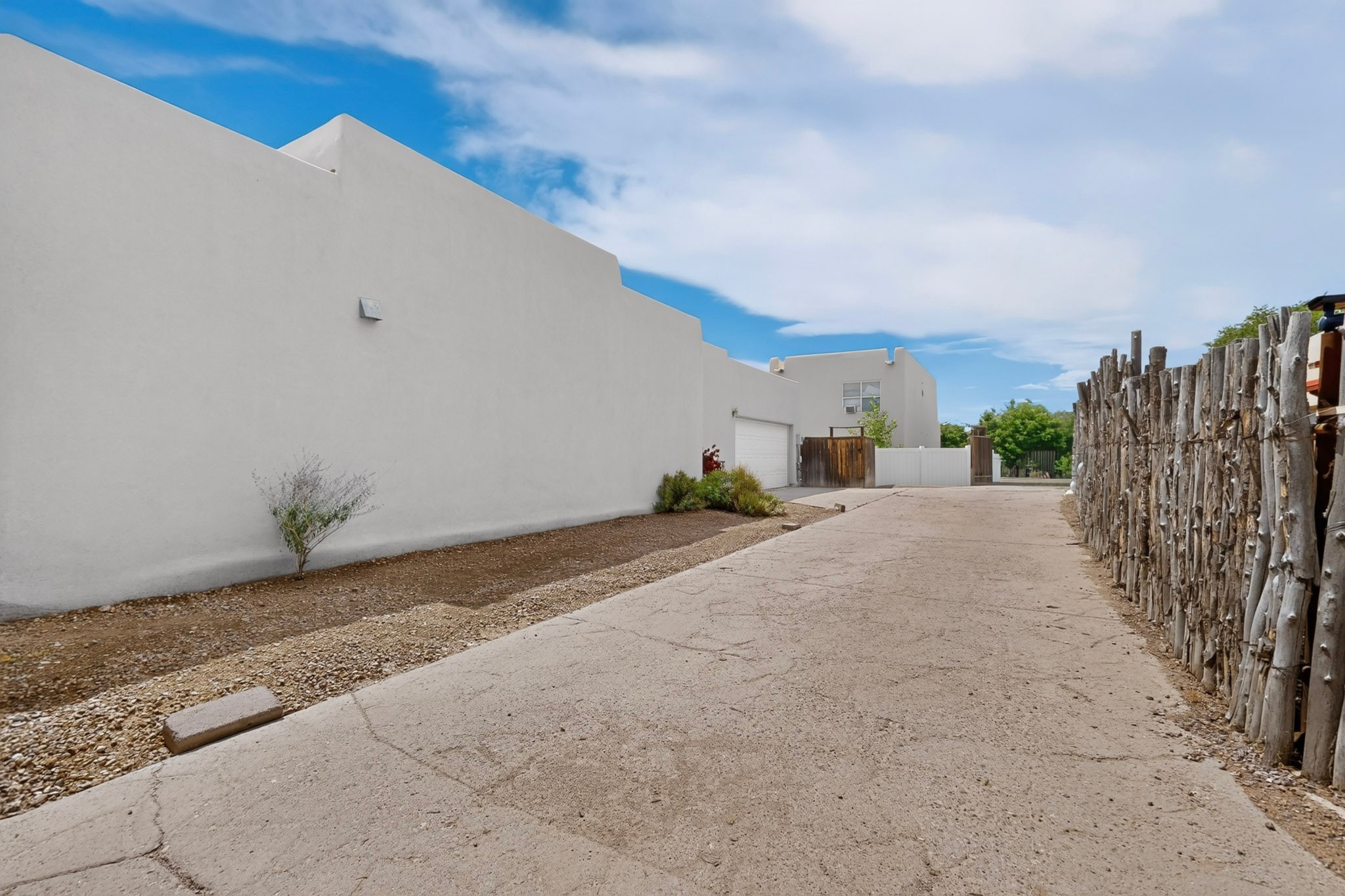 Stucco home with a paved side driveway, garage, and tall rustic wood fence.
