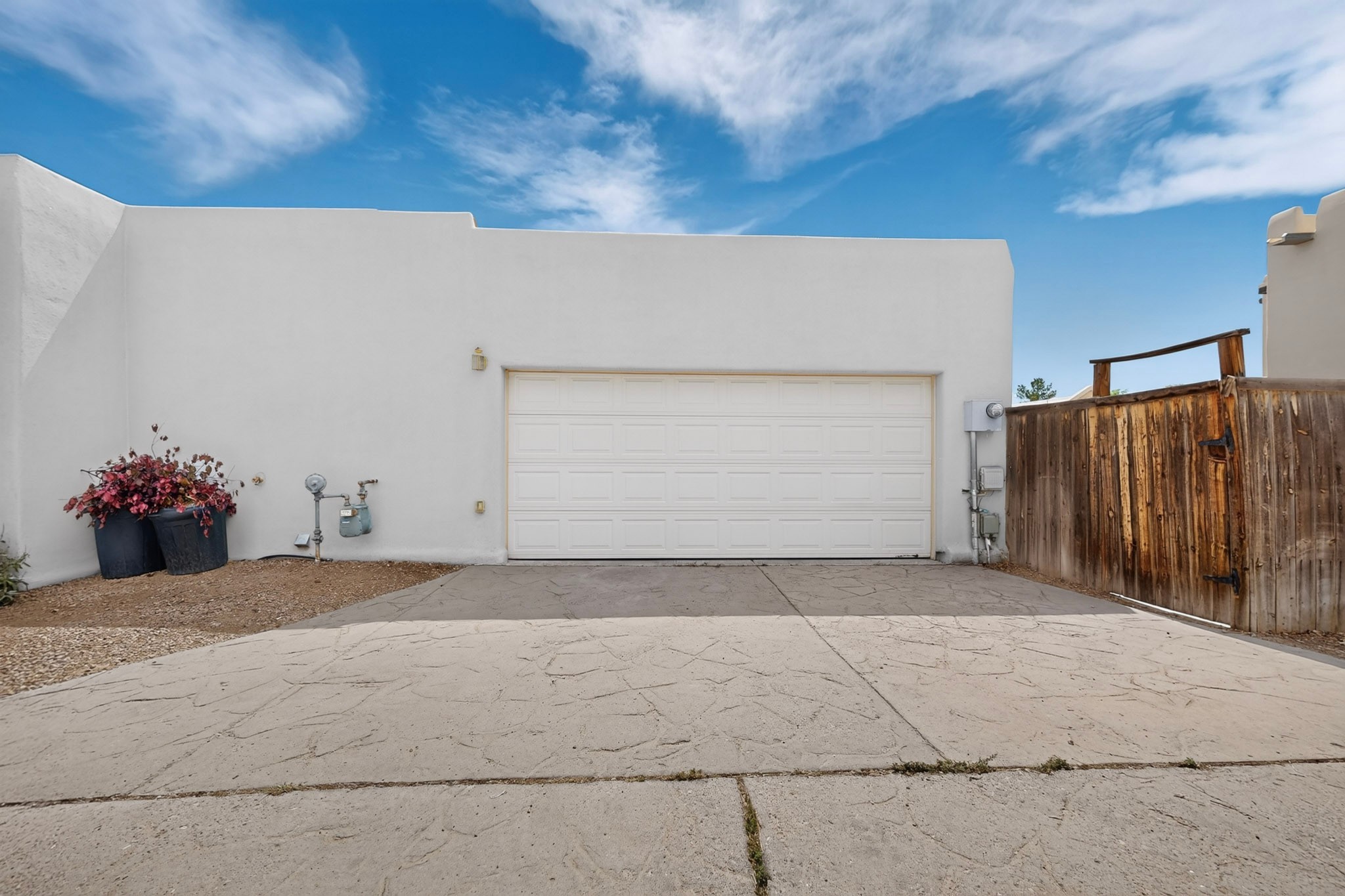 White stucco home with a wide garage door, concrete driveway, and wooden side gate.