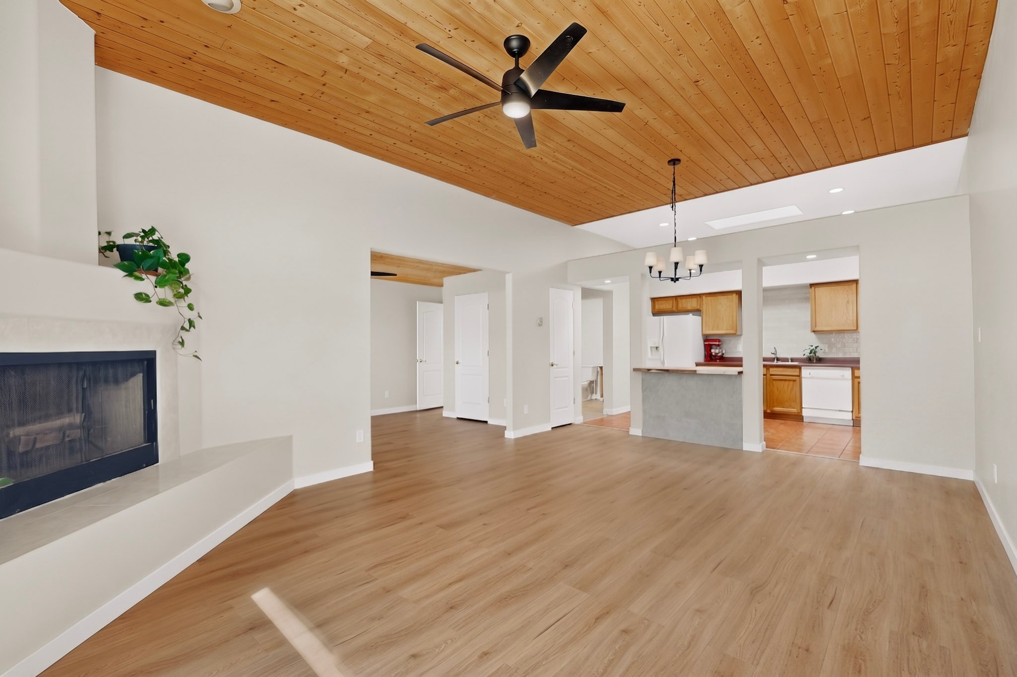 Open living area with a vaulted wood ceiling, fireplace, and kitchen beyond.