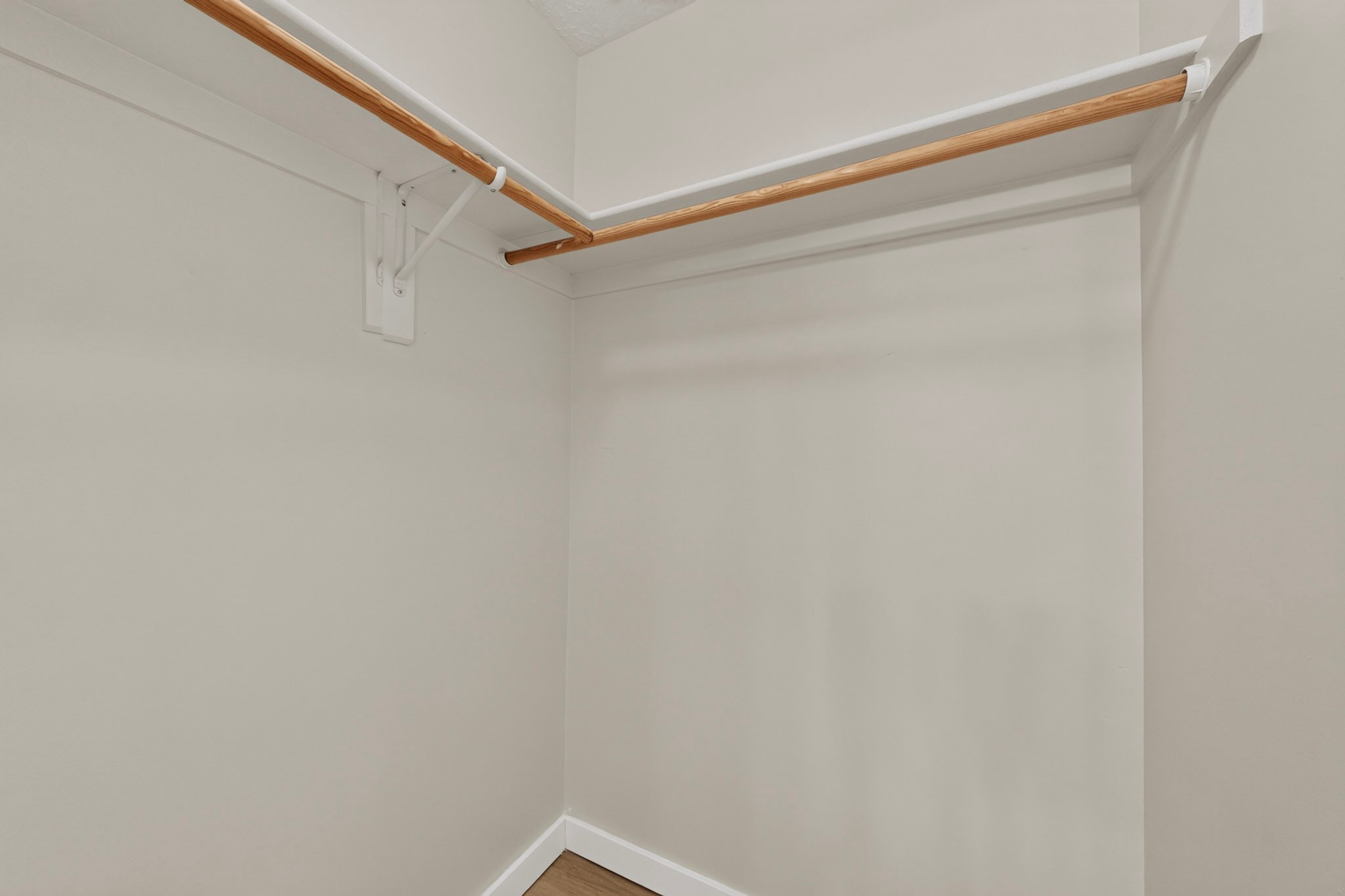 Empty closet with wooden clothes rods and wood flooring.