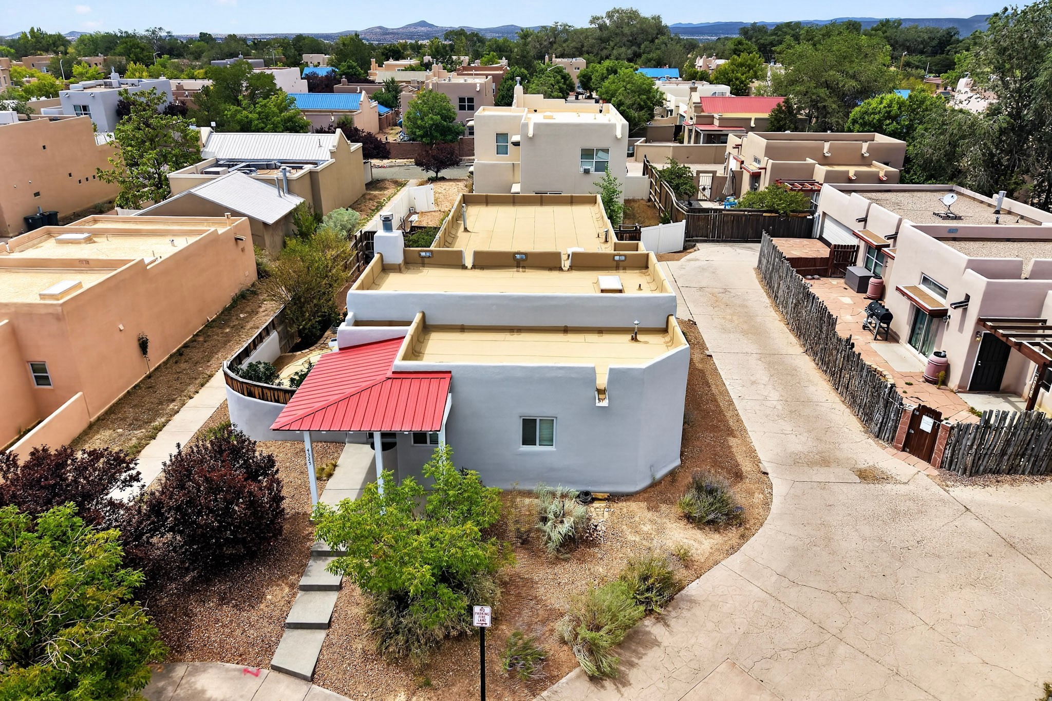 Aerial view of a stucco home with a red metal entry canopy and distant mountains.