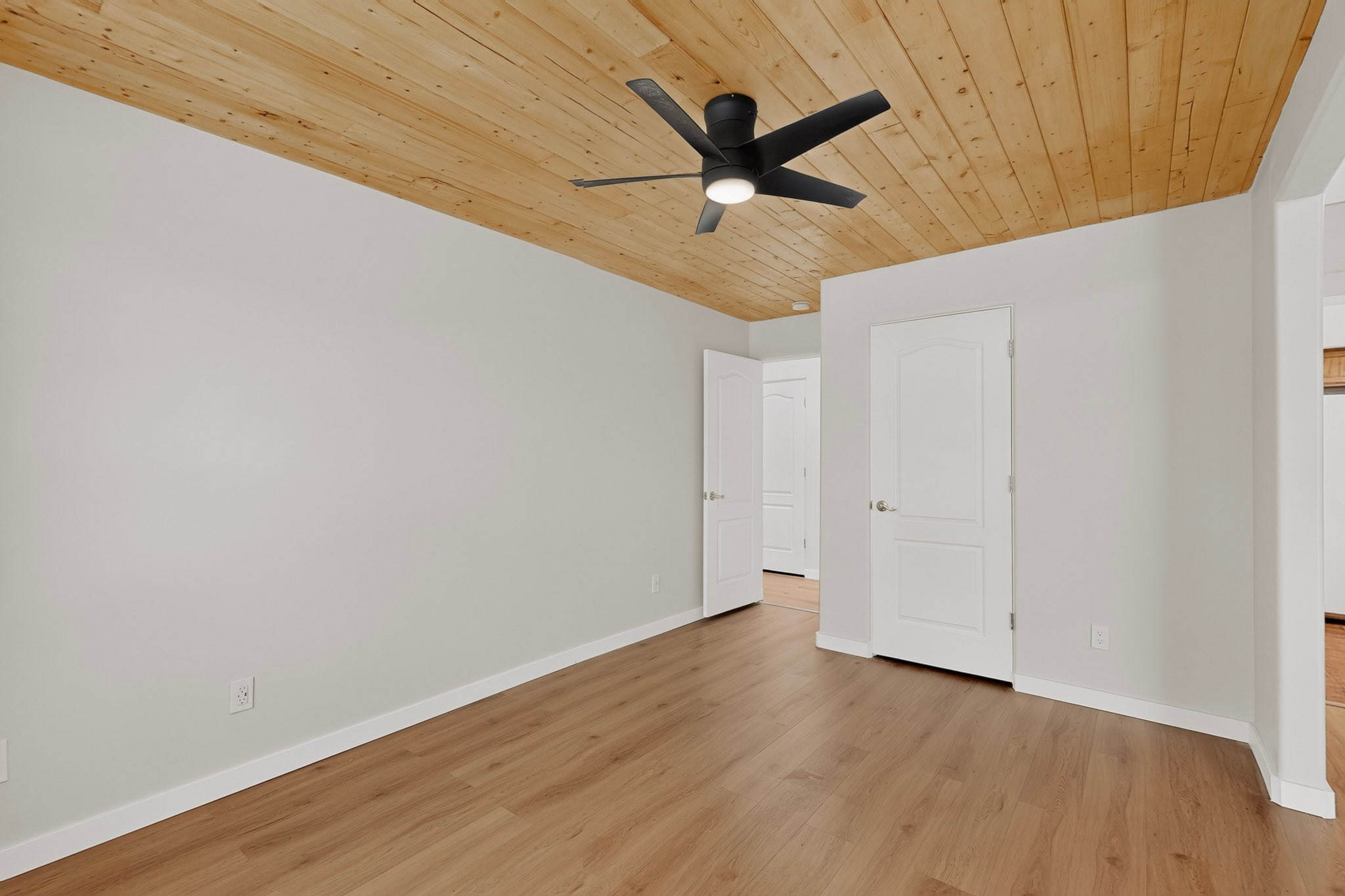 Empty room with wood plank ceiling, black ceiling fan, and two white doors.