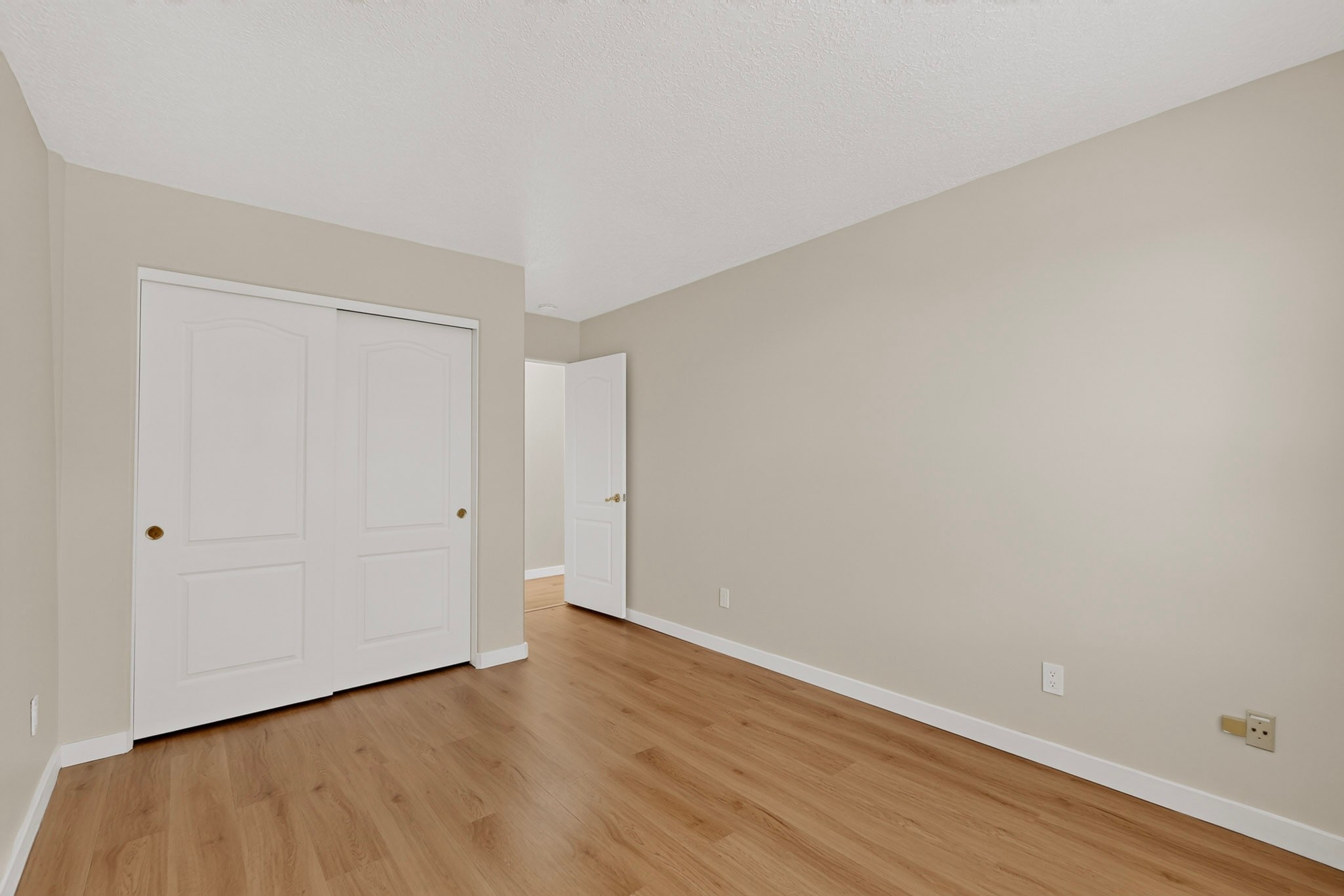 Empty room with wood flooring and white sliding closet doors.