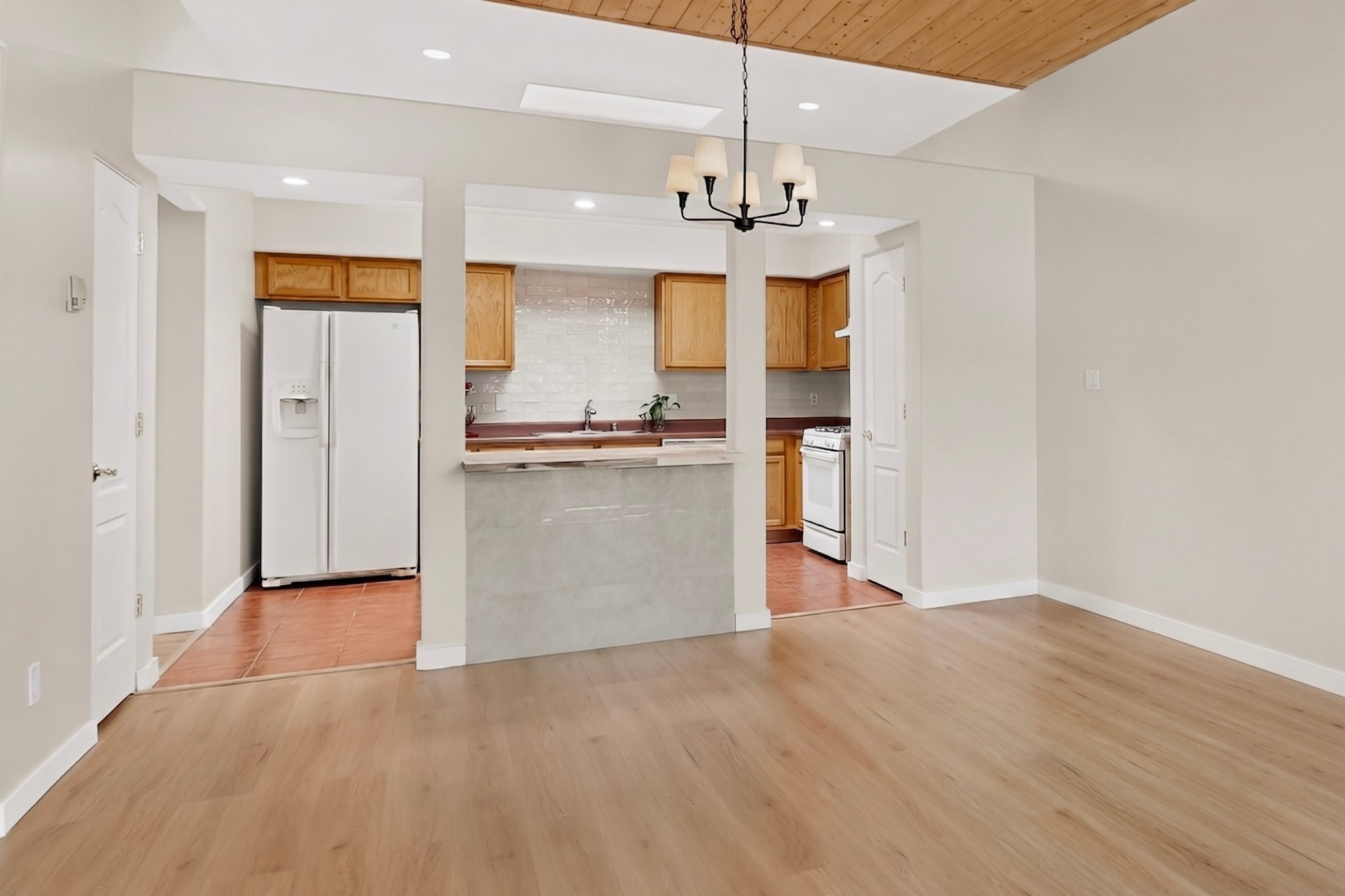 Kitchen with wood cabinets and pass-through bar opening onto an empty dining area.