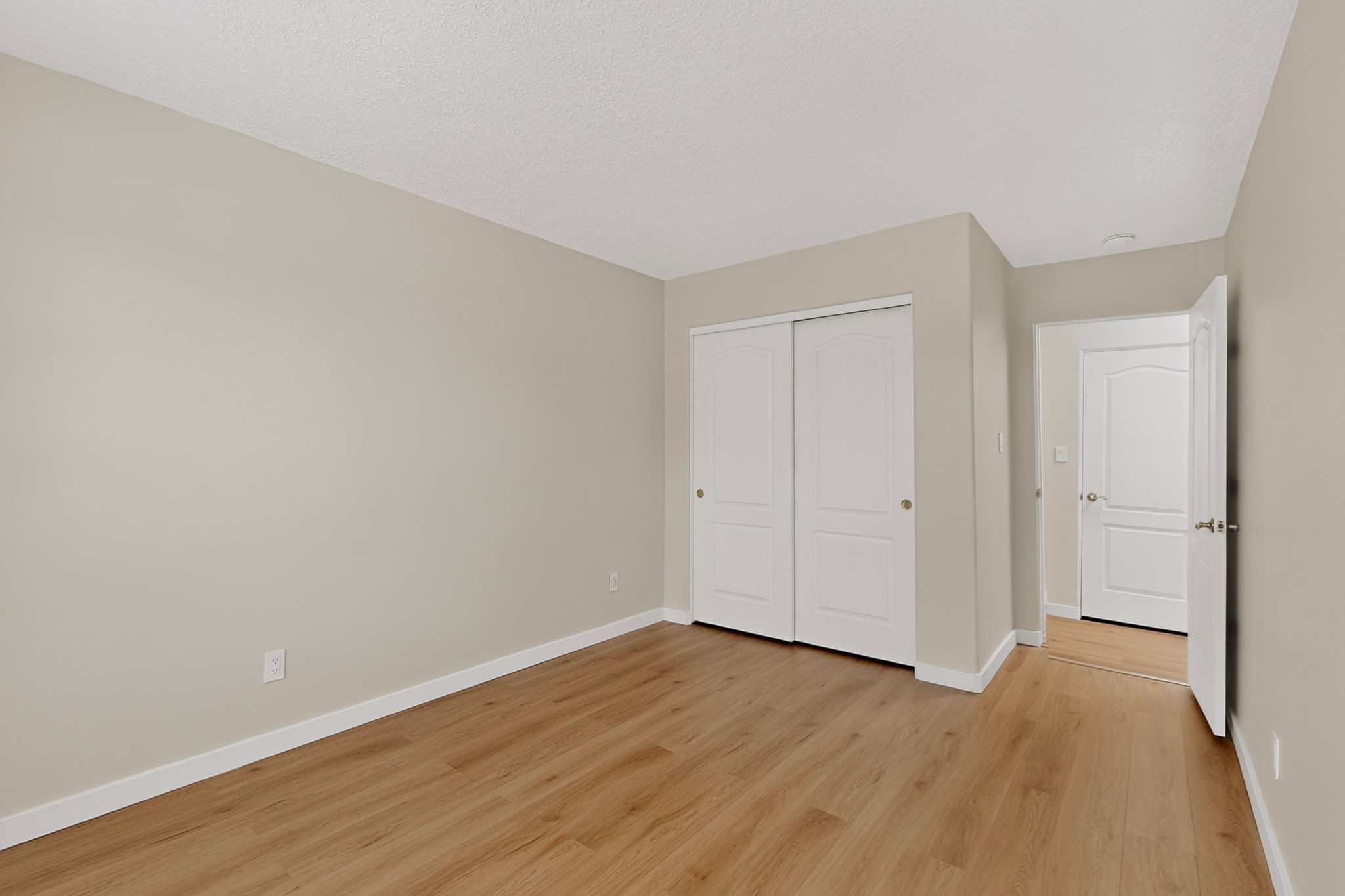 Empty room with light wood flooring, a white double-door closet, and an open doorway.
