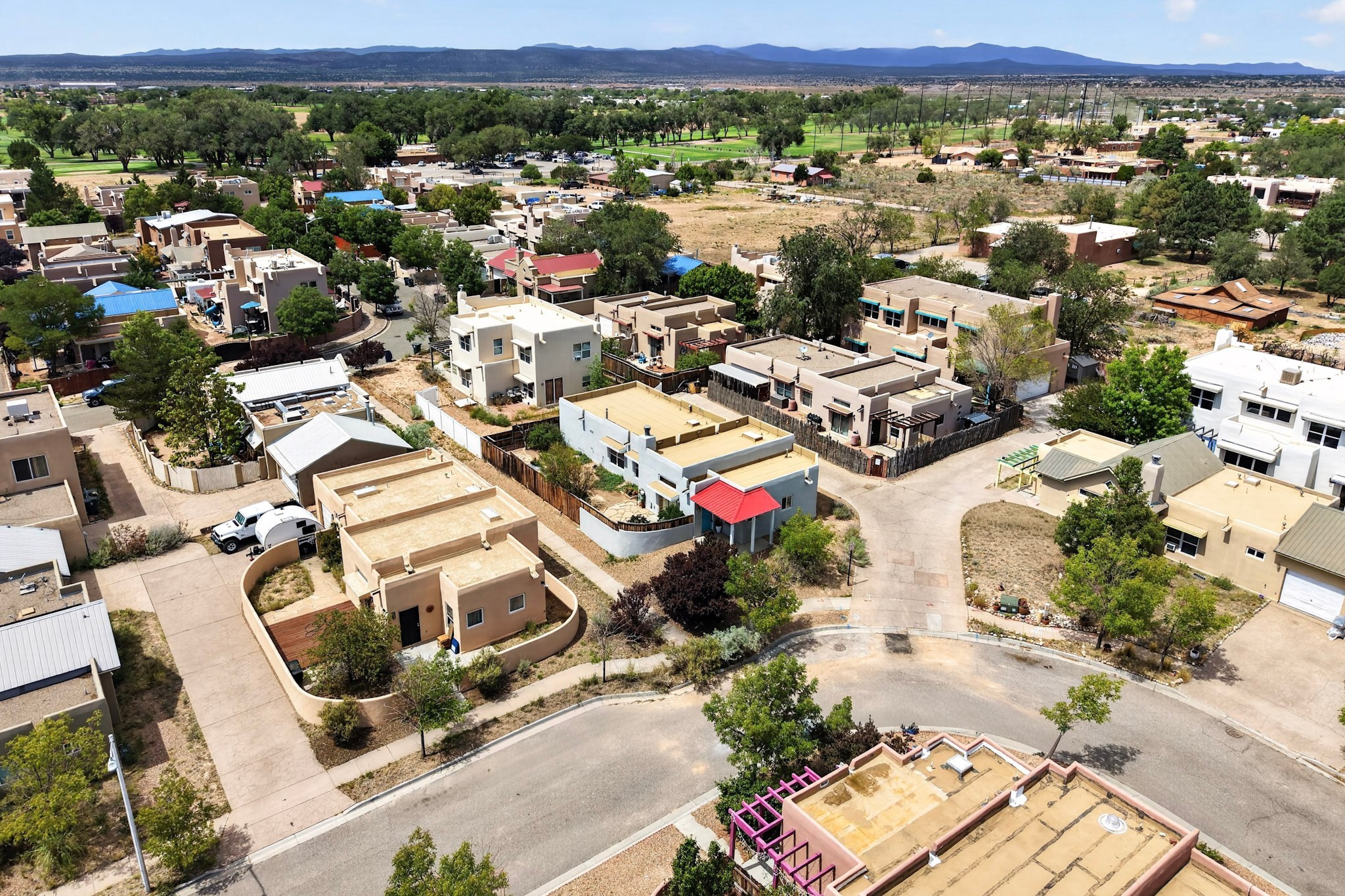 Aerial neighborhood view with adobe-style homes, green golf course, and distant mountains.