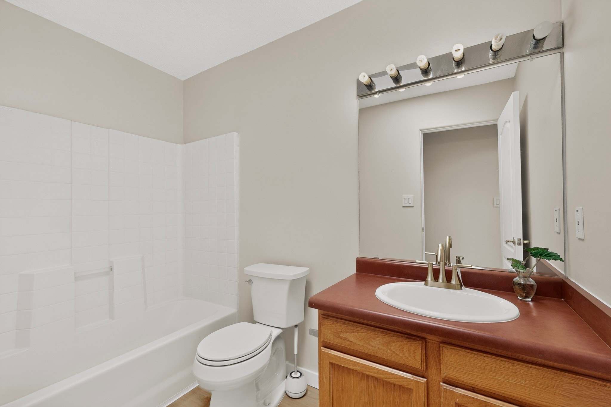 Bathroom with a white tub and shower, toilet, and wood vanity with a reddish-brown countertop.