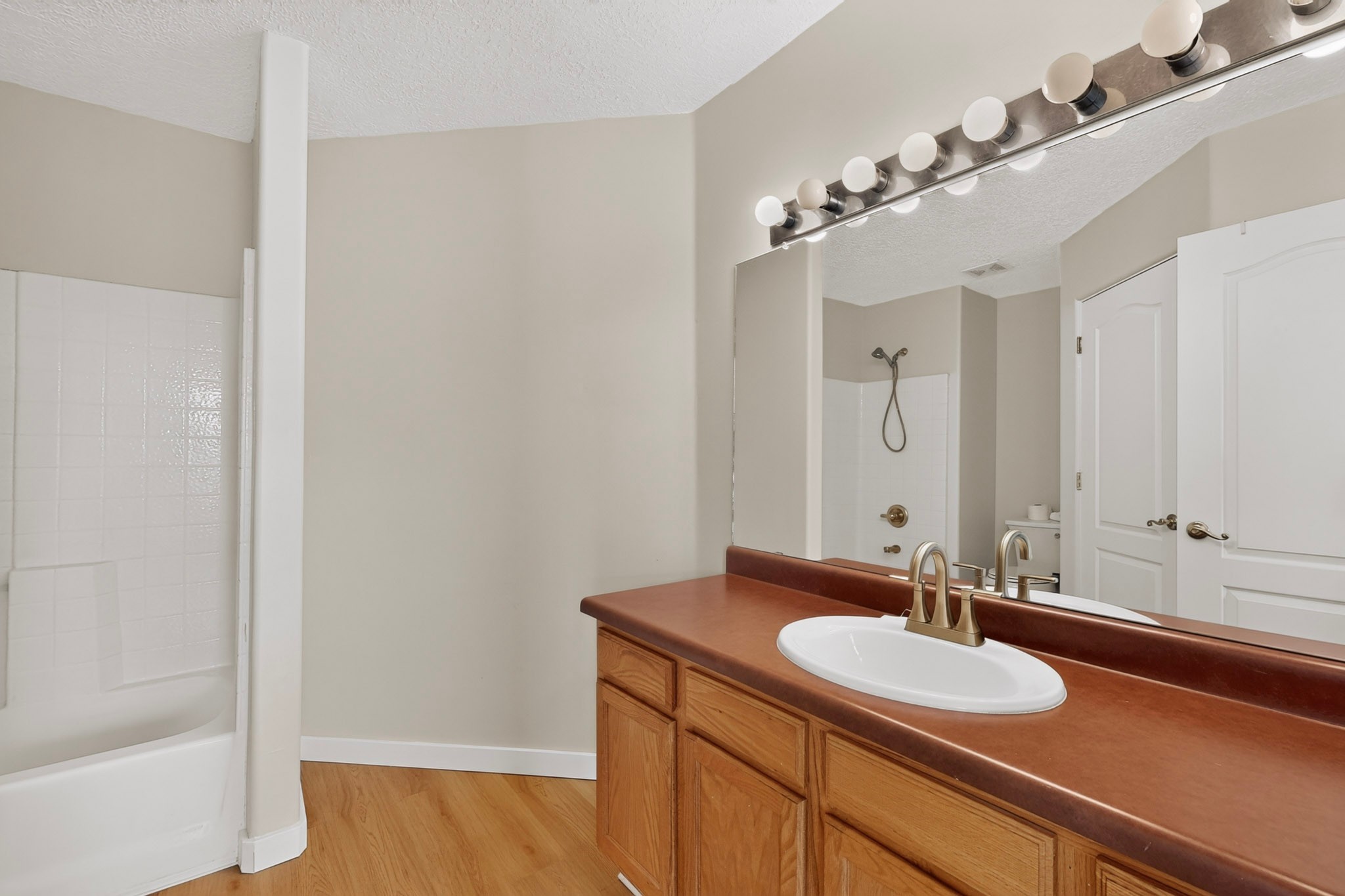 Bathroom with a white tub, tiled shower, and wood vanity with a reddish-brown countertop.