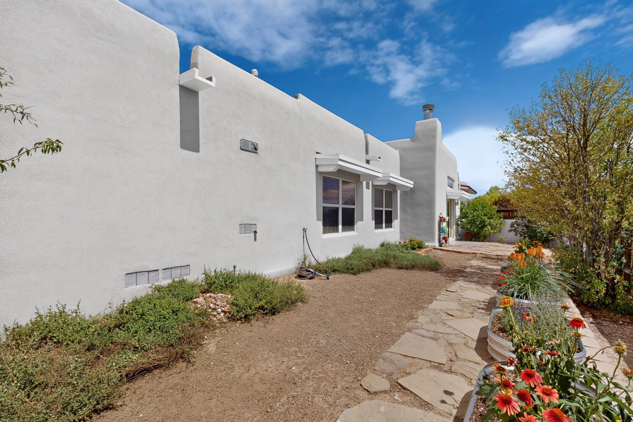 White stucco home beside a stone walkway and raised flower beds.