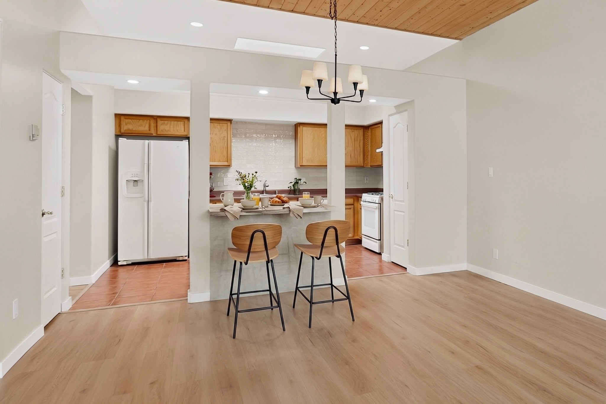 Kitchen with a breakfast bar, two stools, warm wood cabinets, and a wood-paneled ceiling accent.