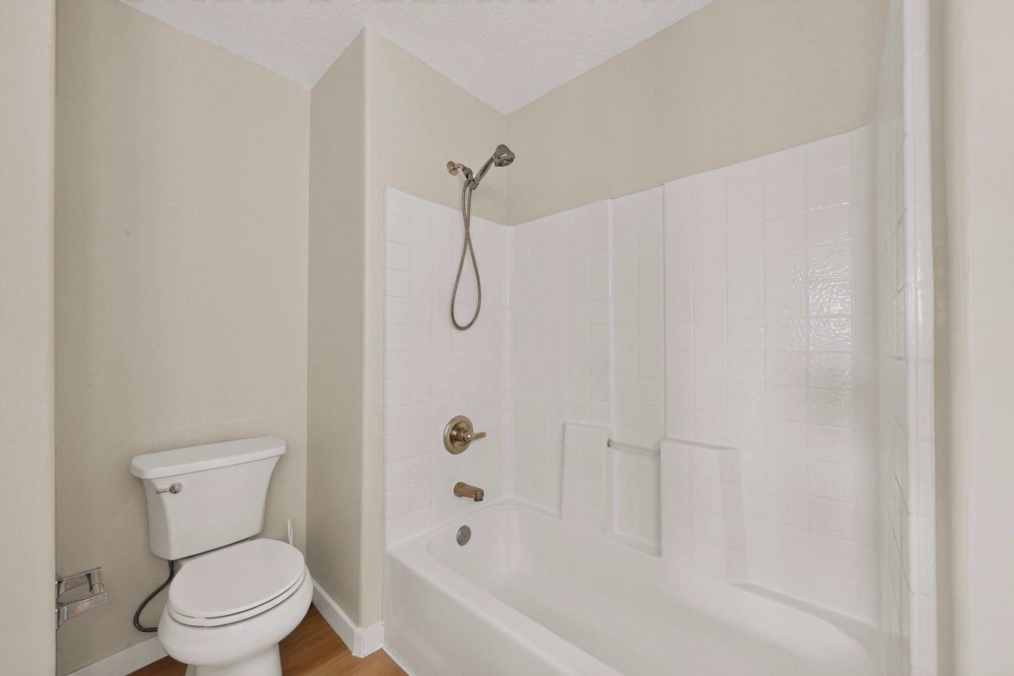 Bathroom with a white tiled tub and shower, bronze fixtures, and a toilet.