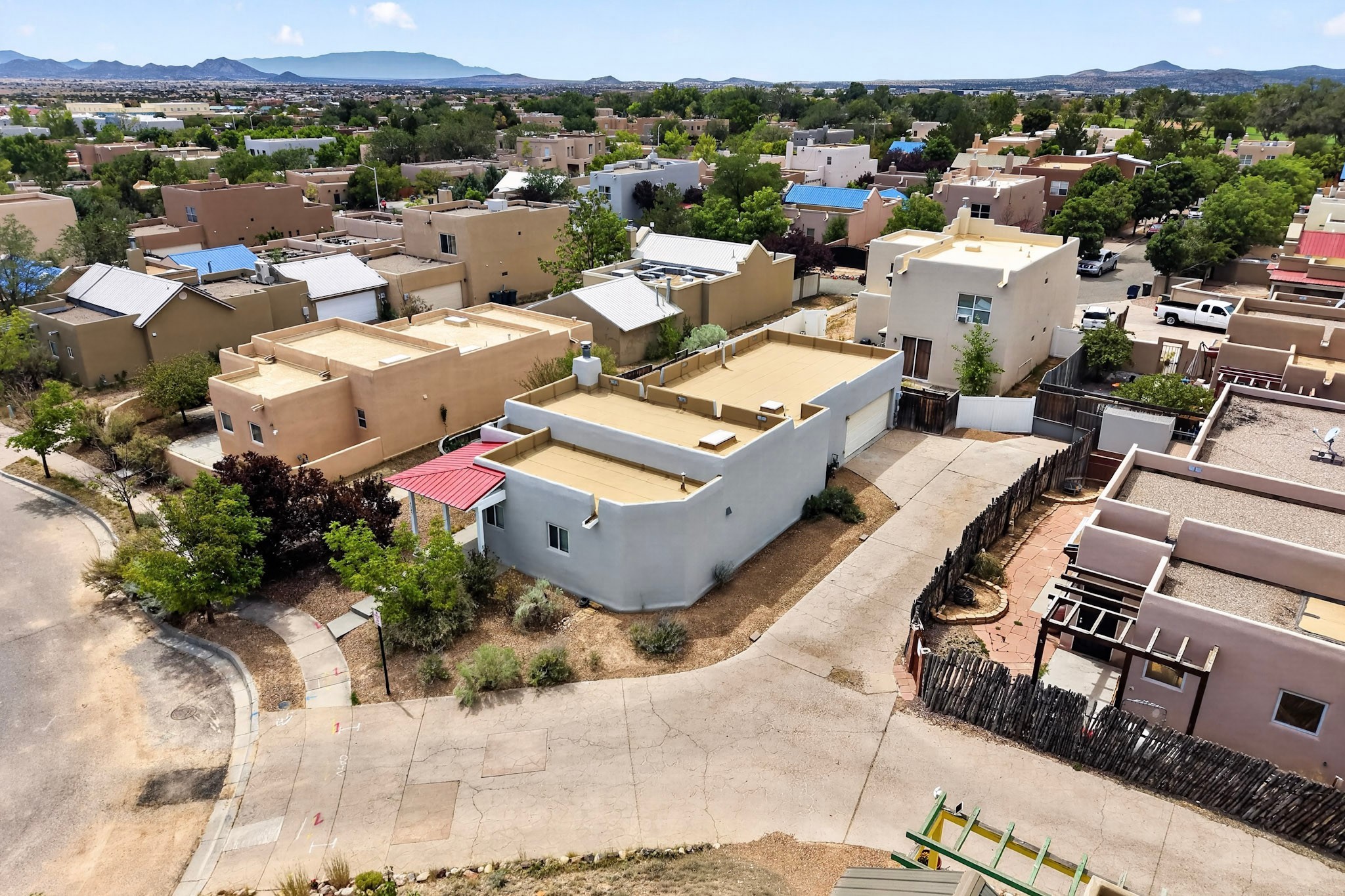 Aerial view of a gray stucco home with a flat roof and red awning, with mountains in the distance.