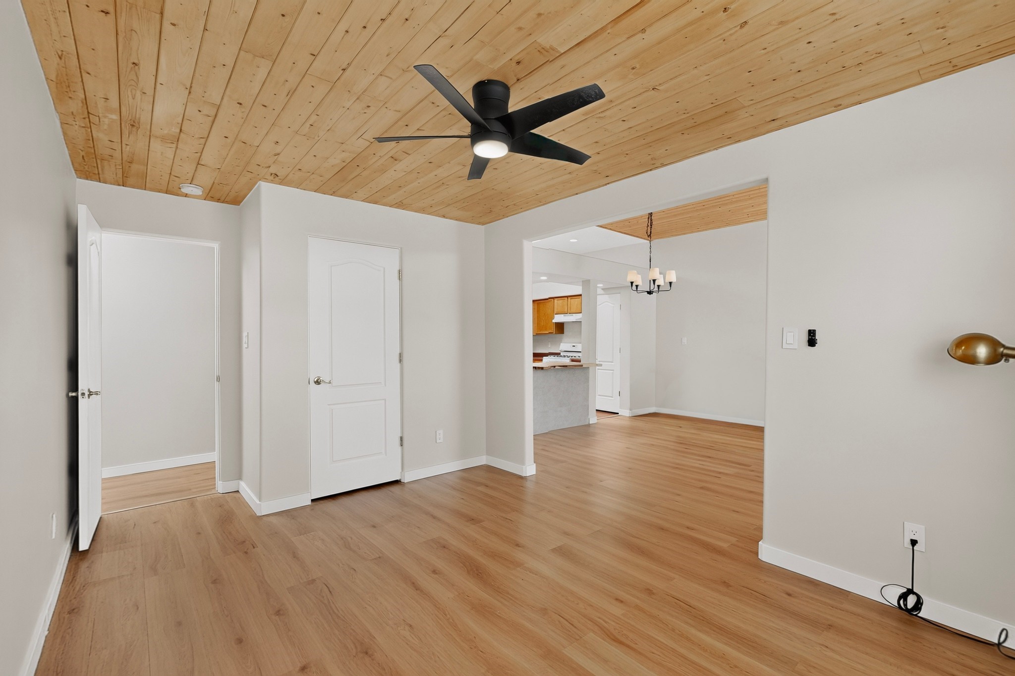 Open living and dining area with wood-plank ceiling, wood floors, and a black ceiling fan.