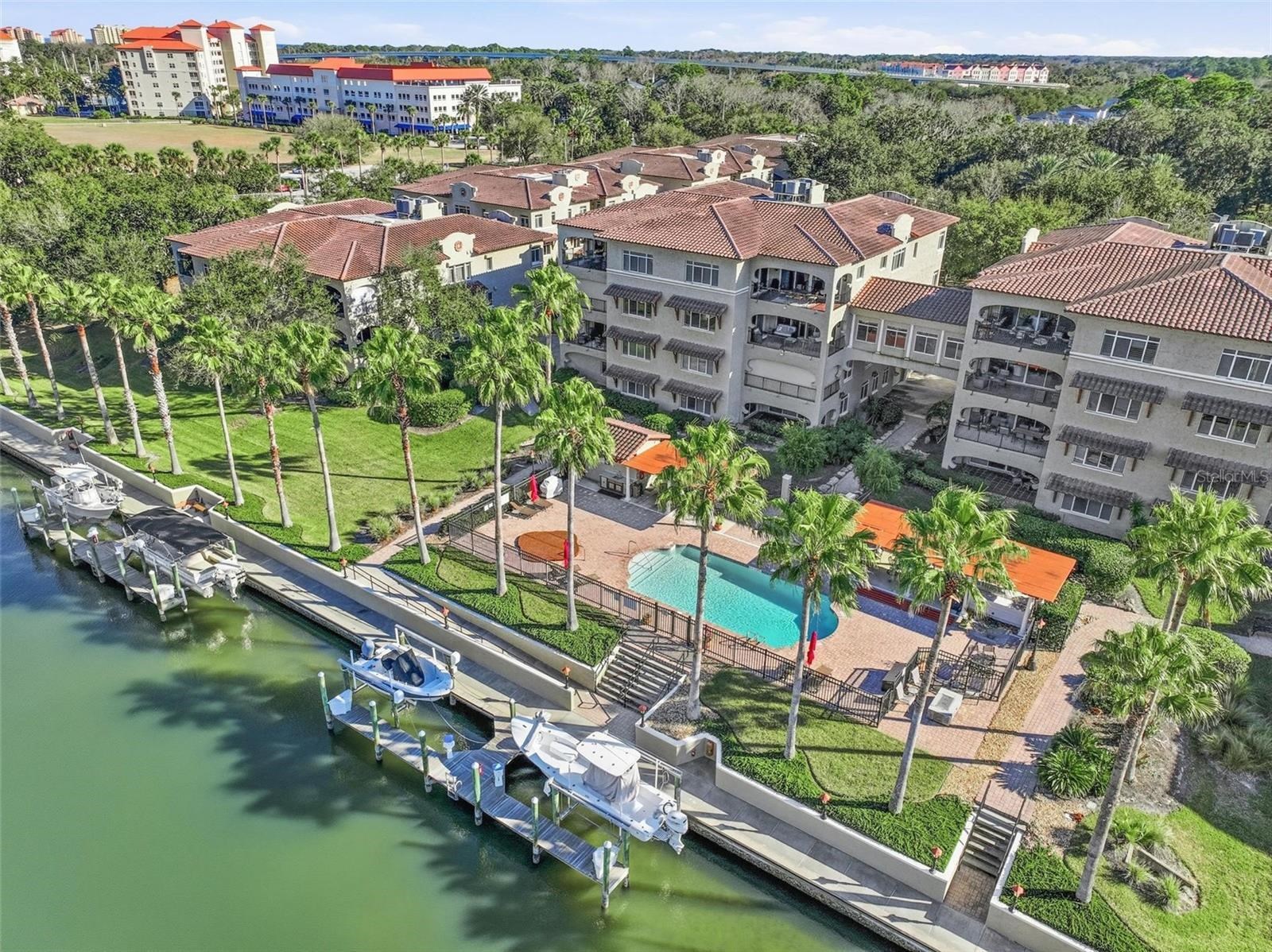 Waterfront condominium complex with a palm-lined pool and boats docked along the canal