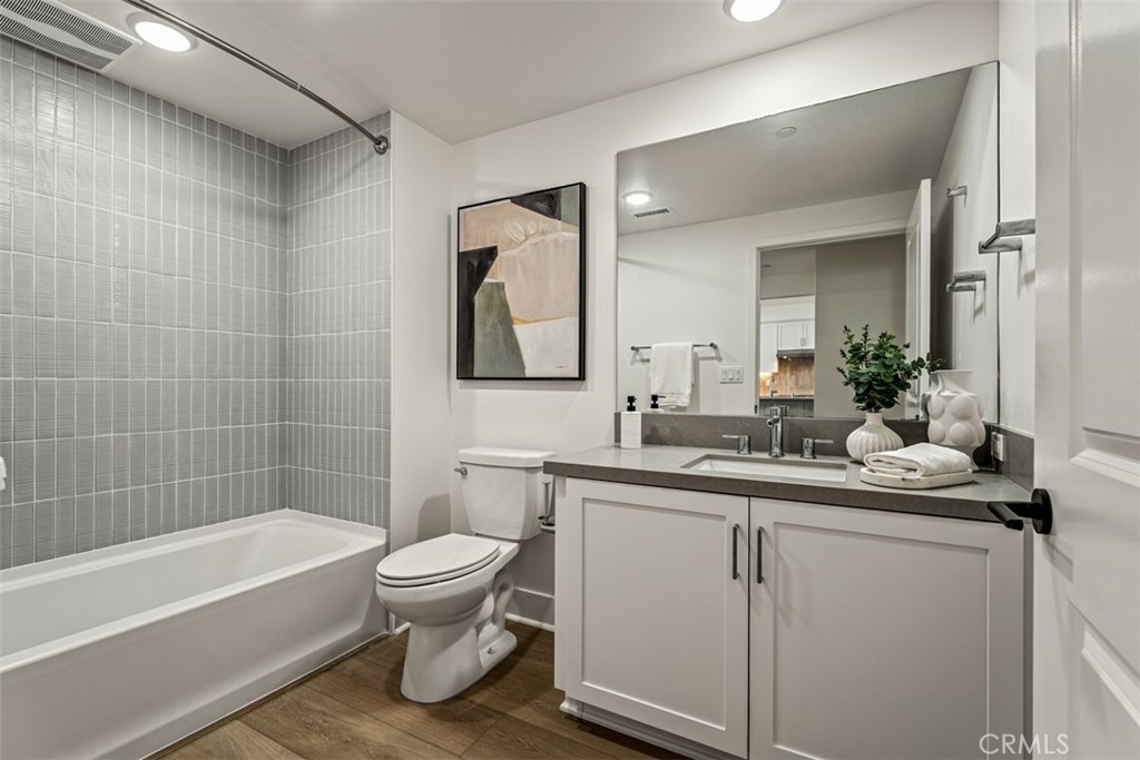 Bathroom with gray tiled tub surround, toilet, and white double vanity.