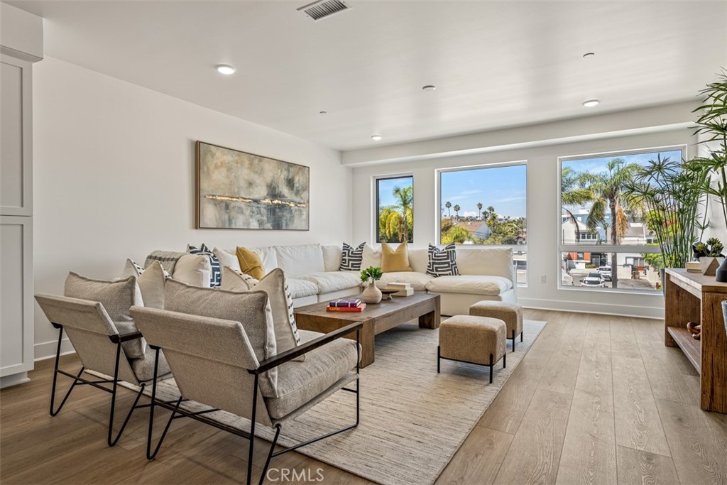Staged living room with a white sectional, two accent chairs, and large windows overlooking palm trees.