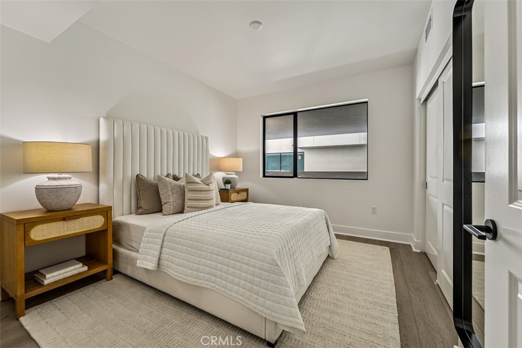 Staged bedroom with a tall upholstered headboard, neutral bedding, and a window facing a neighboring building.