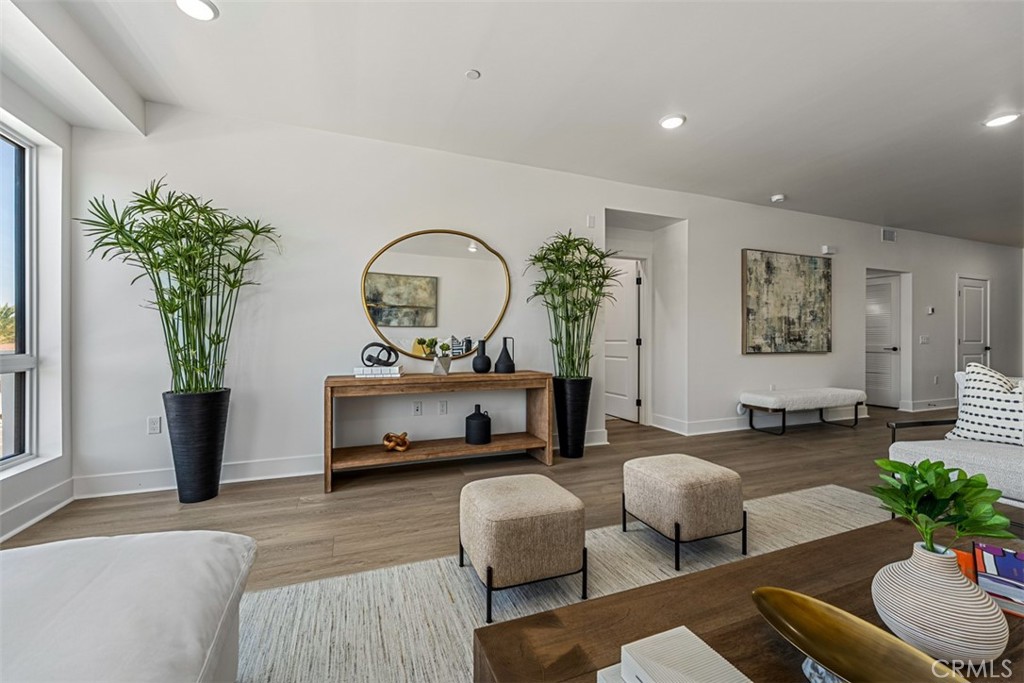 Staged living room with a wood console, round mirror, potted palms, and upholstered ottomans.