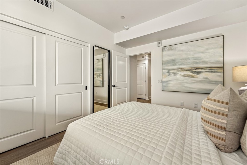 Staged bedroom with a white quilted bed, paneled closet doors, and a large abstract seascape painting.