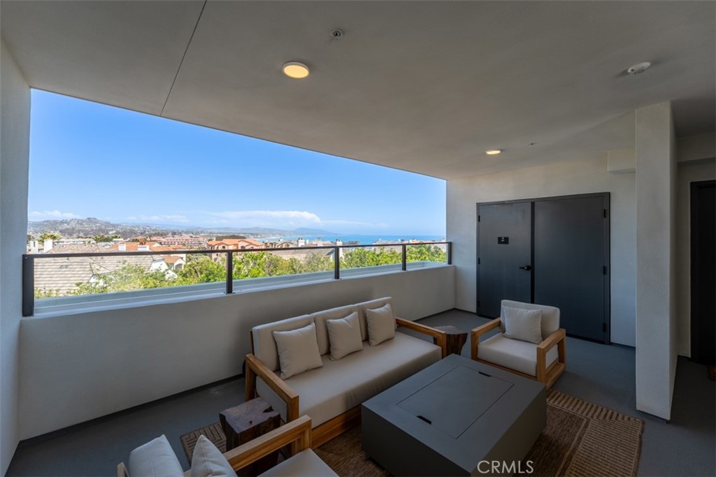 Covered balcony with lounge seating overlooking rooftops, hills, and the ocean.
